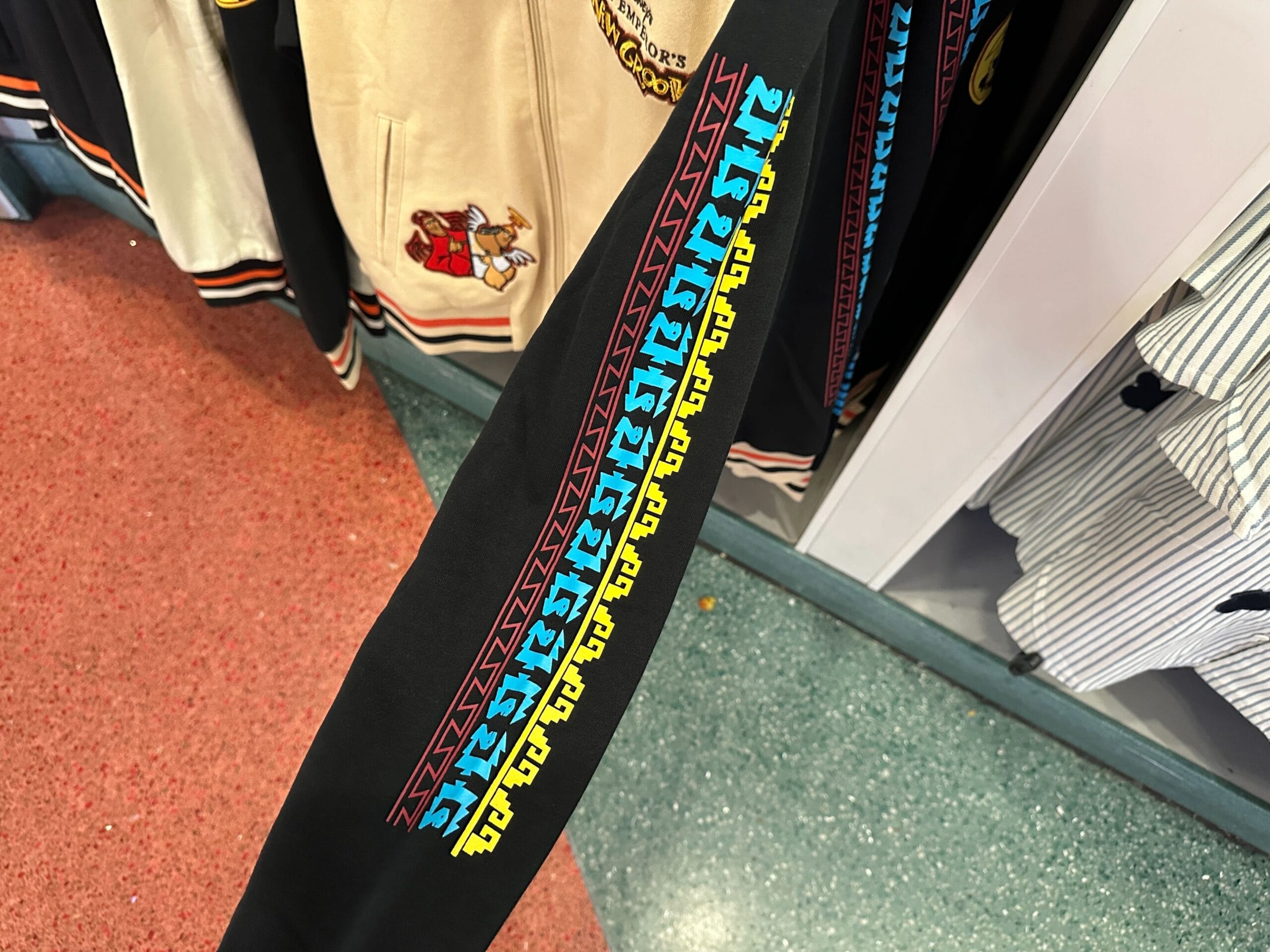 A black sleeve evokes Disney Letterman Jackets with colorful "Hogwarts" text repeated in blue and yellow along the length.