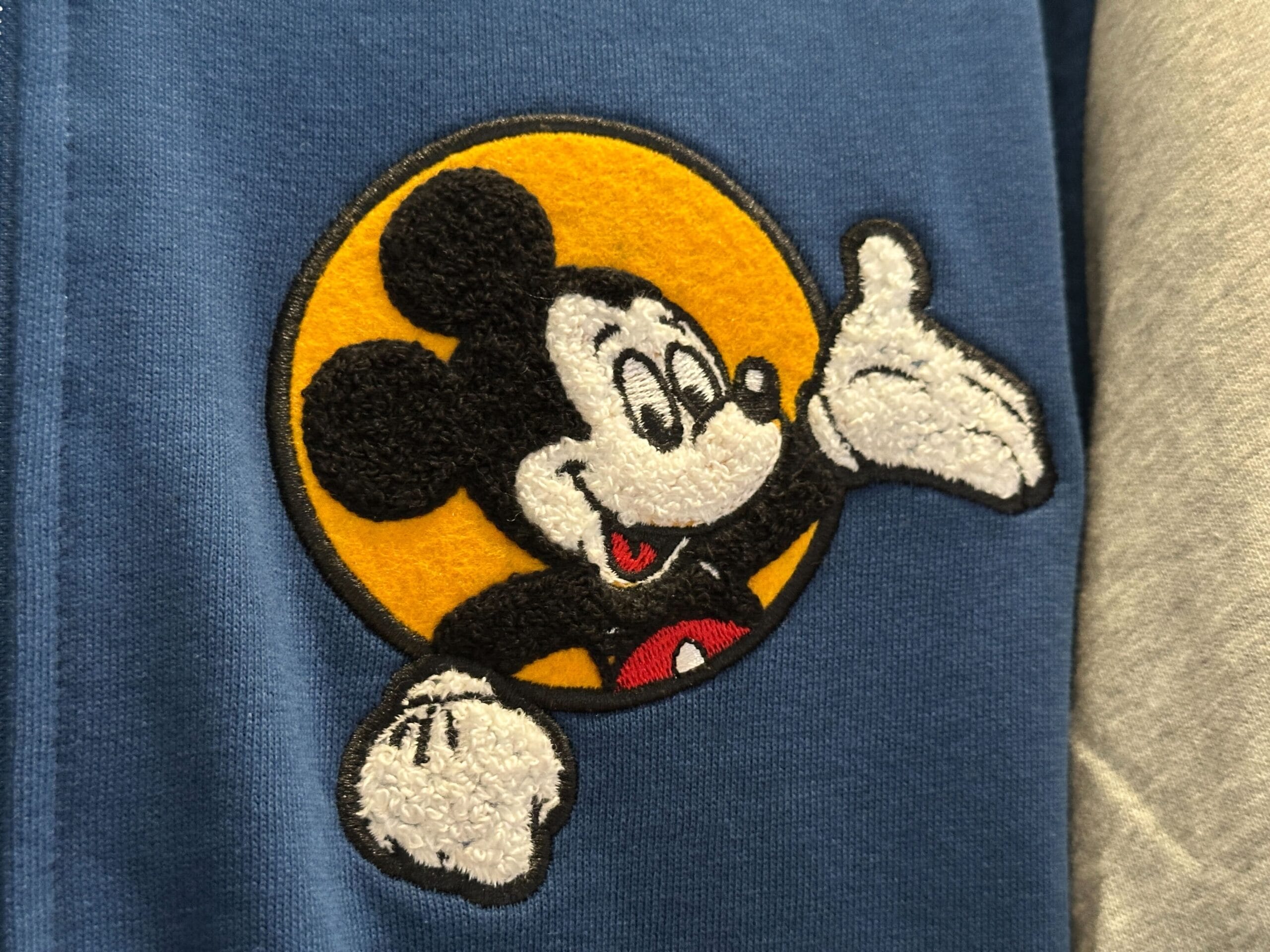 Embroidered patch of Mickey Mouse waving, inspired by Walt Disney World, on blue fabric with a yellow circle behind him.