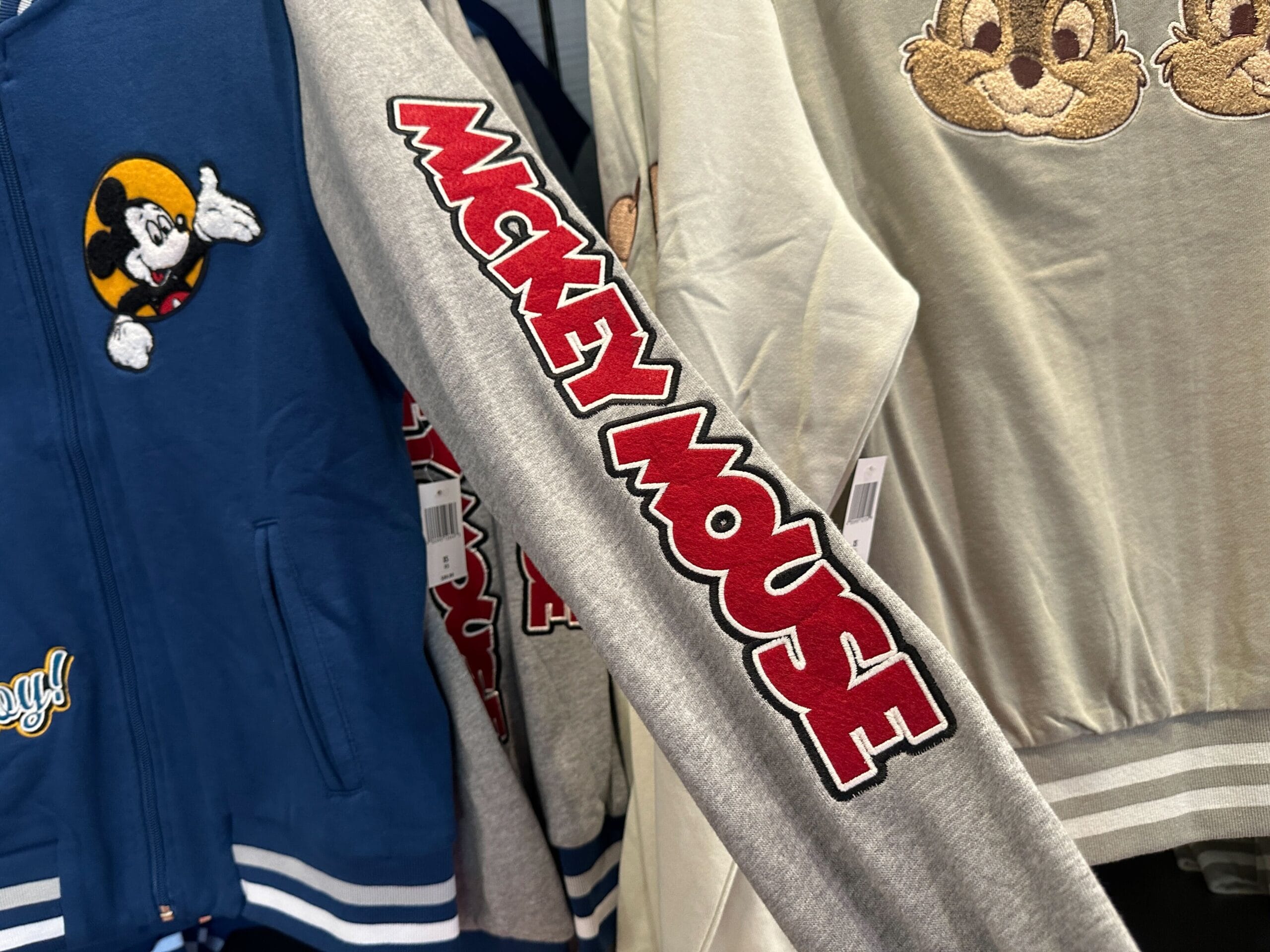 Gray sleeve with bold red and black "Mickey Mouse" text, next to blue Disney letterman jackets and light gray character styles.