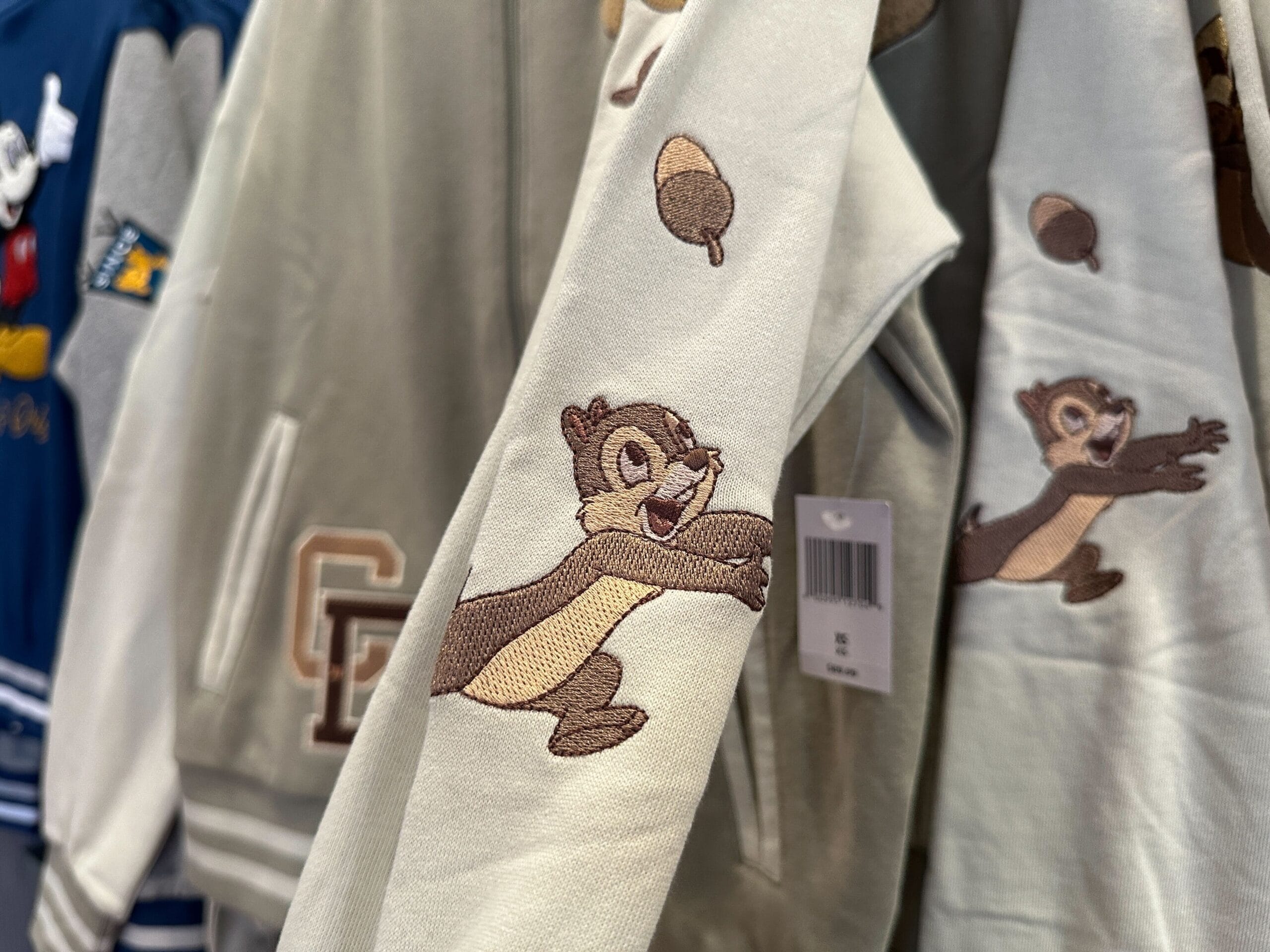 Close-up of a Disney Letterman Jacket sleeve with Chip and Dale reaching for an acorn, embroidered on light fabric in a store.