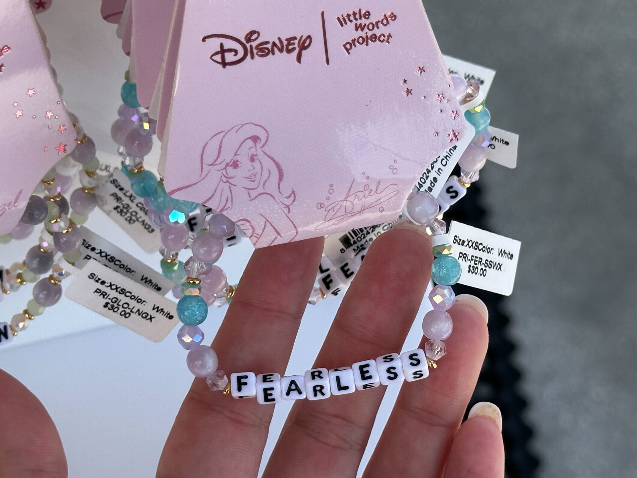 A hand holds a beaded Disney bracelet that spells "FEARLESS" with letter beads.