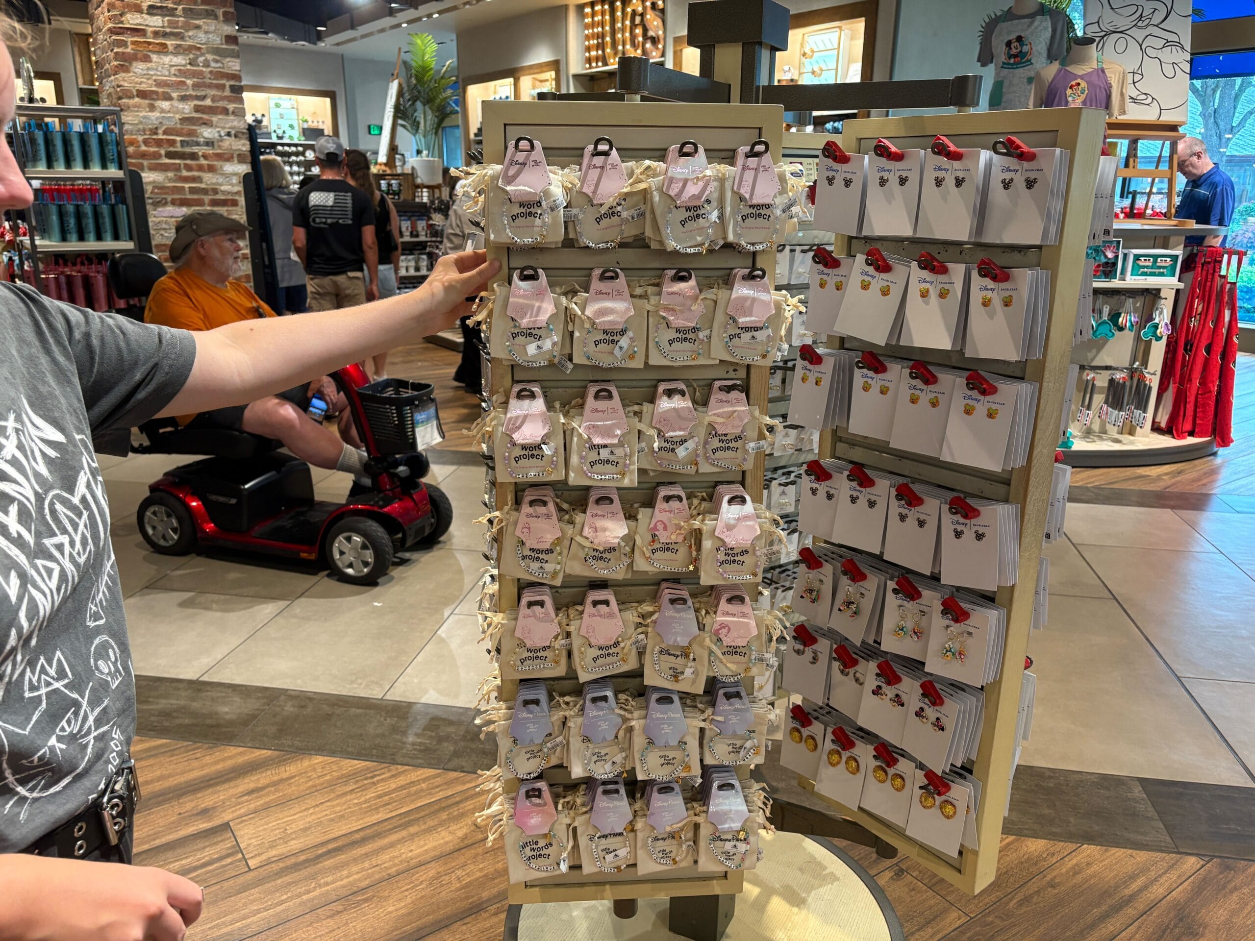 A person looks at souvenirs on a rotating display stand in a store, with pins and keychains arranged neatly.