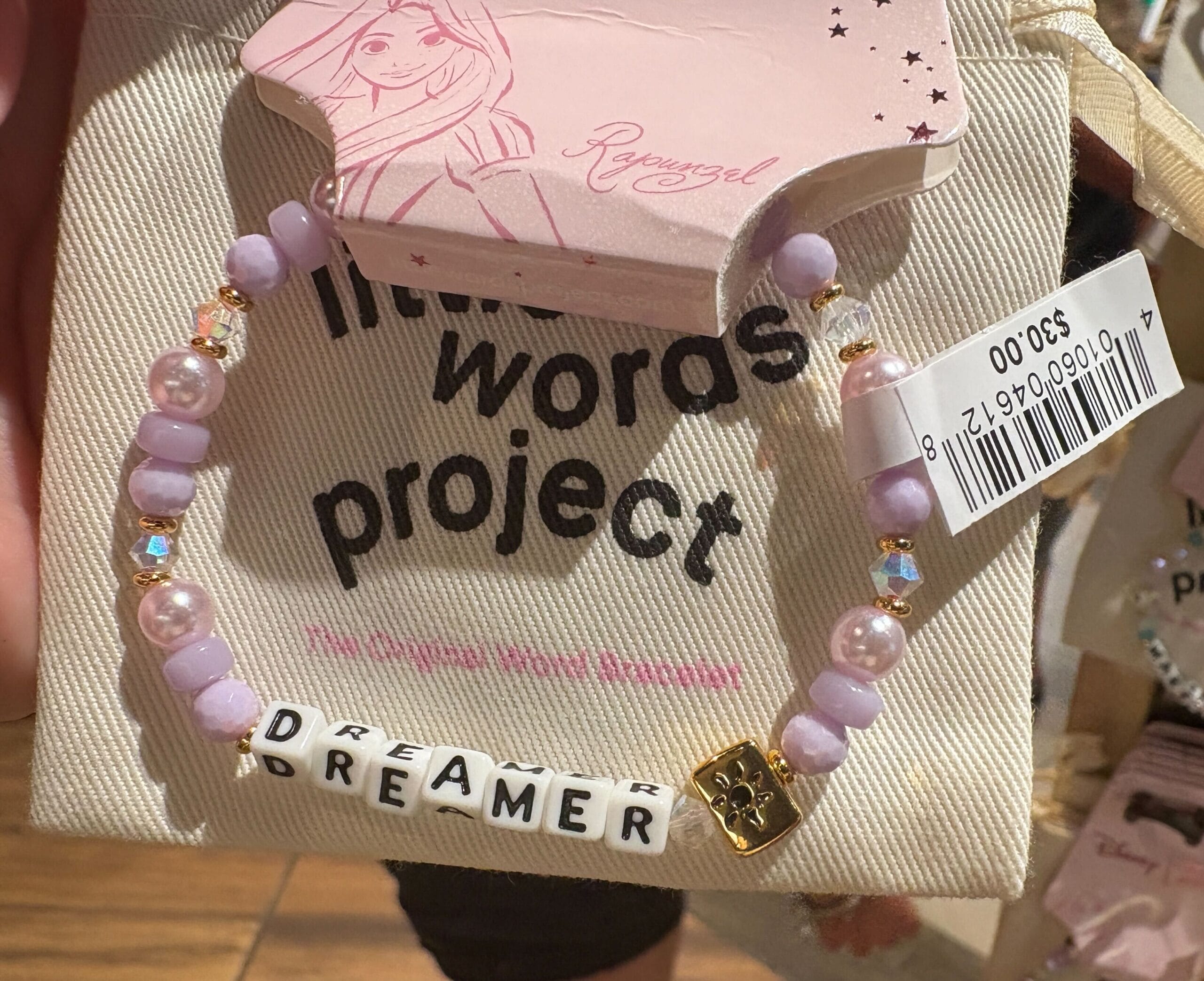 A beaded bracelet with “DREAMER” letter beads, displayed on Rapunzel-themed "Little Words Project" packaging.