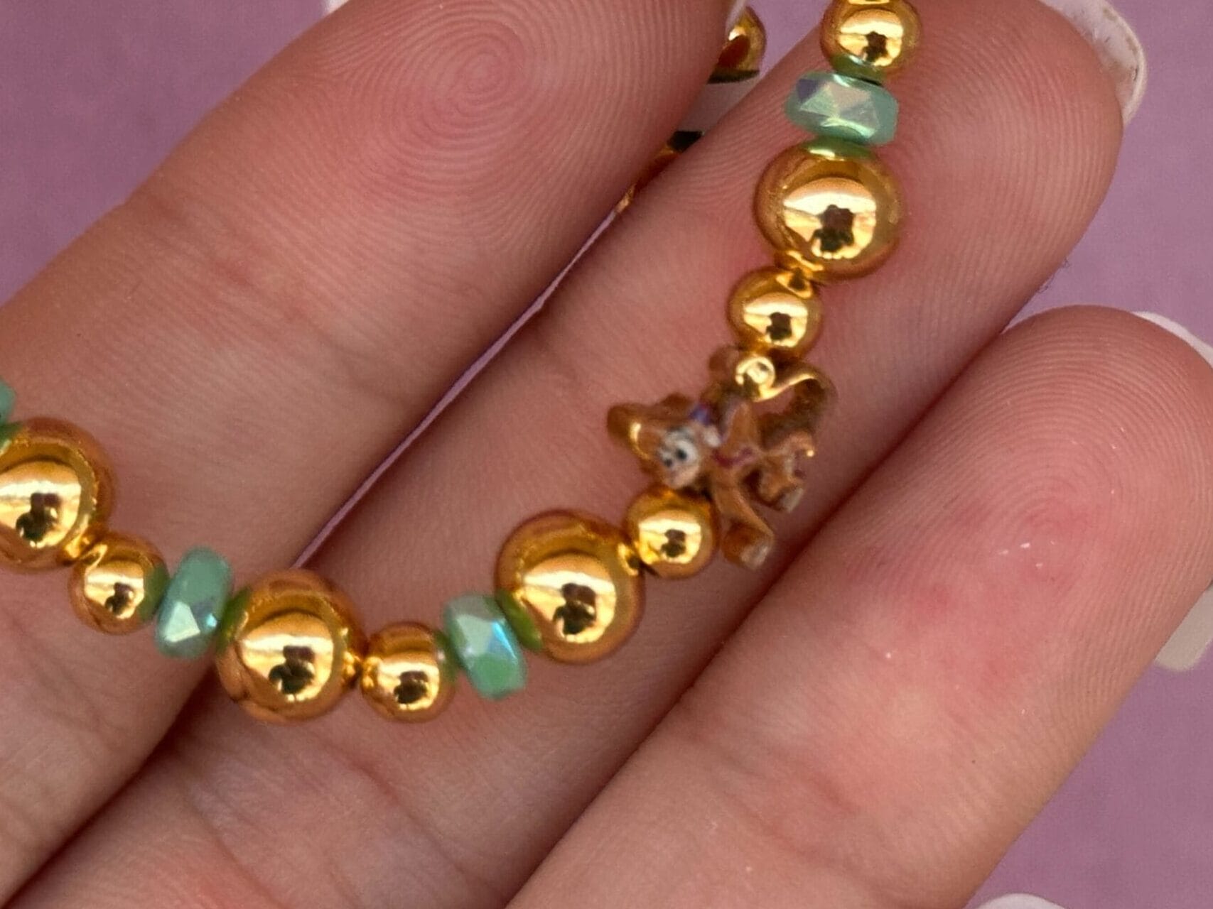 Gold and green beaded bracelet with a small starfish charm held between fingers with manicured nails.