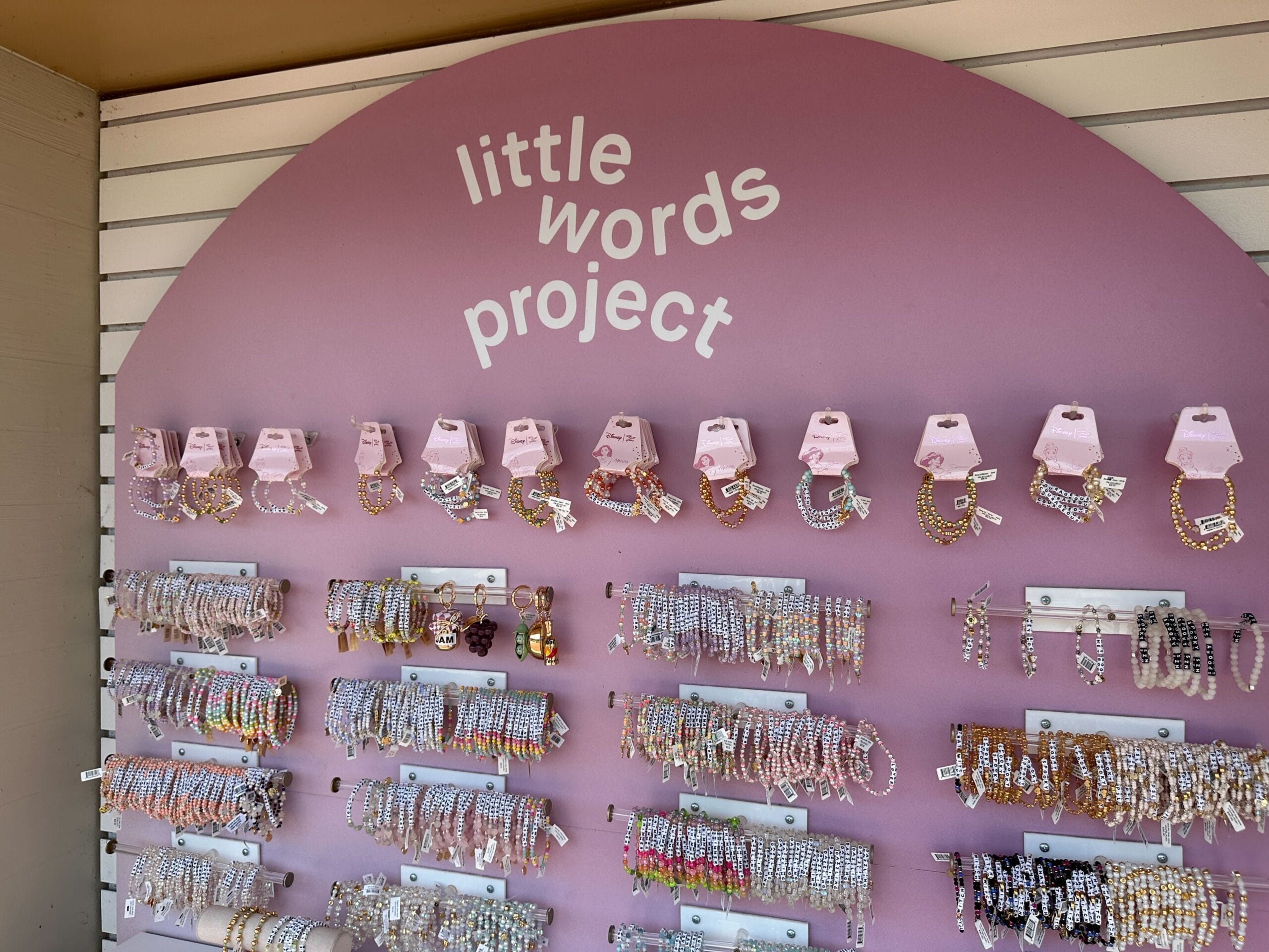 A display of colorful beaded bracelets and keychains under a sign reading "little words project" on a purple background.