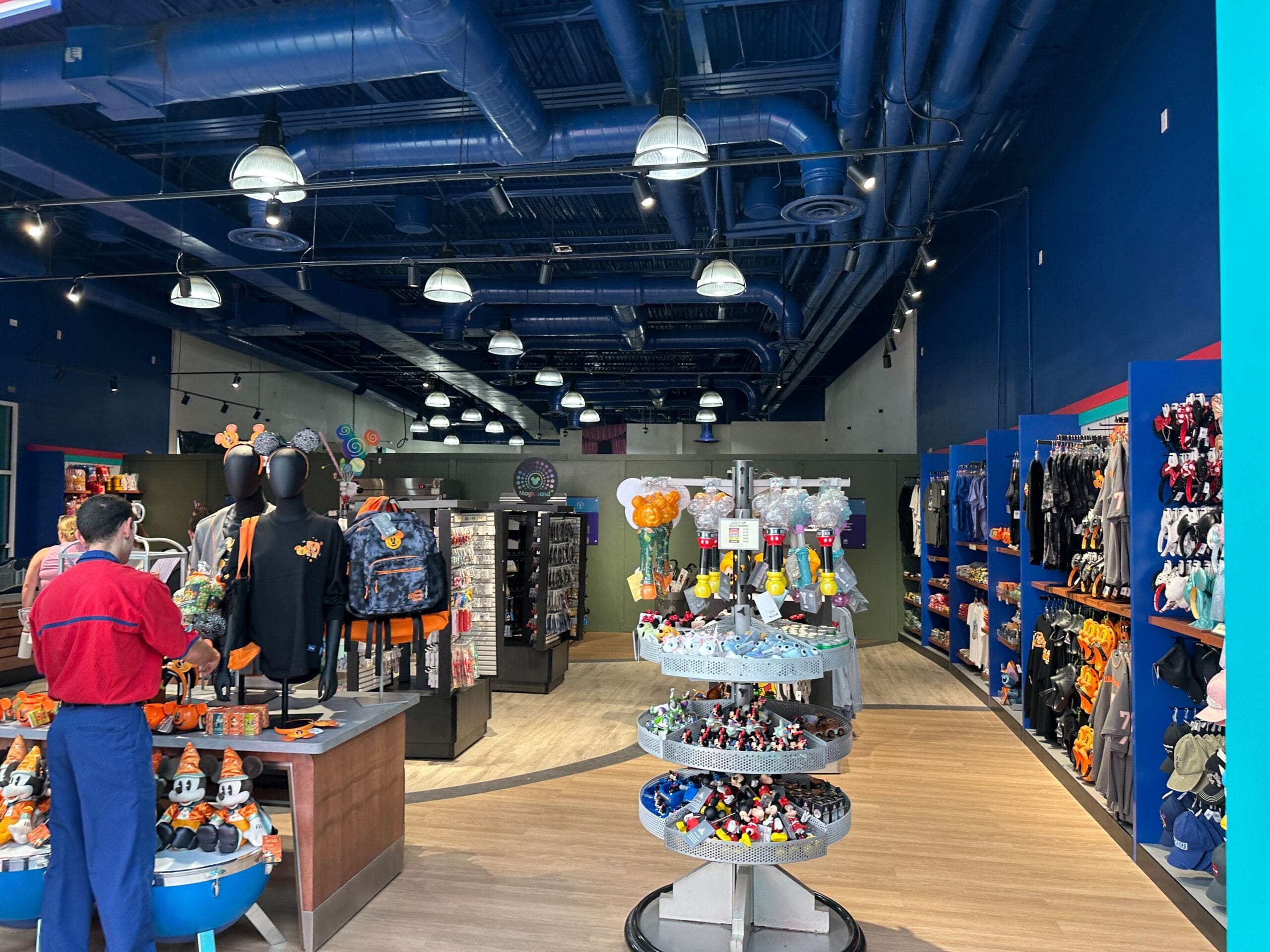 A brightly lit store with shelves of toys, plushies, clothes, and accessories; two people stand near the entrance.