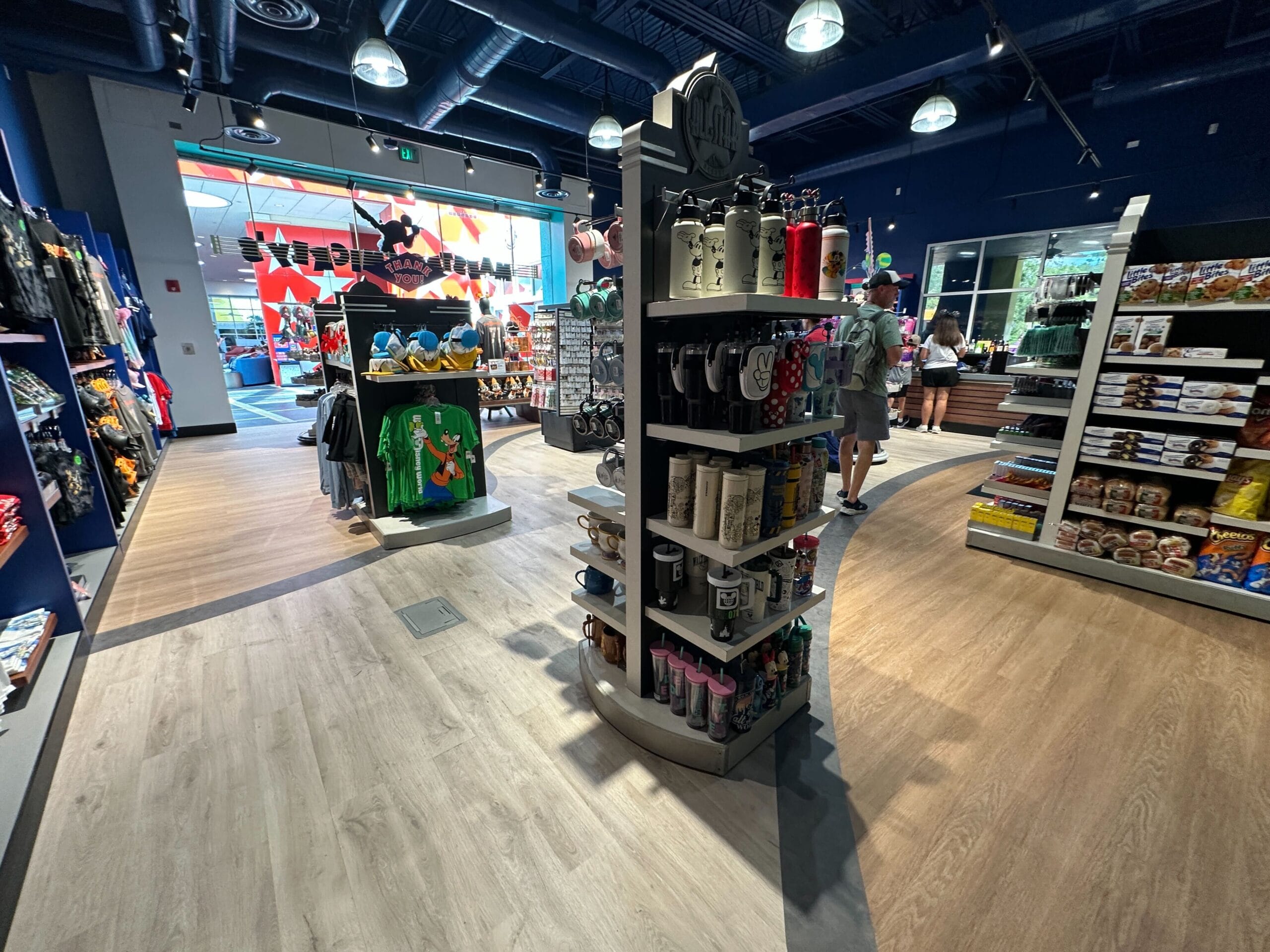 A retail store interior with shelves displaying various merchandise, including bottles, mugs, clothing, and snacks.