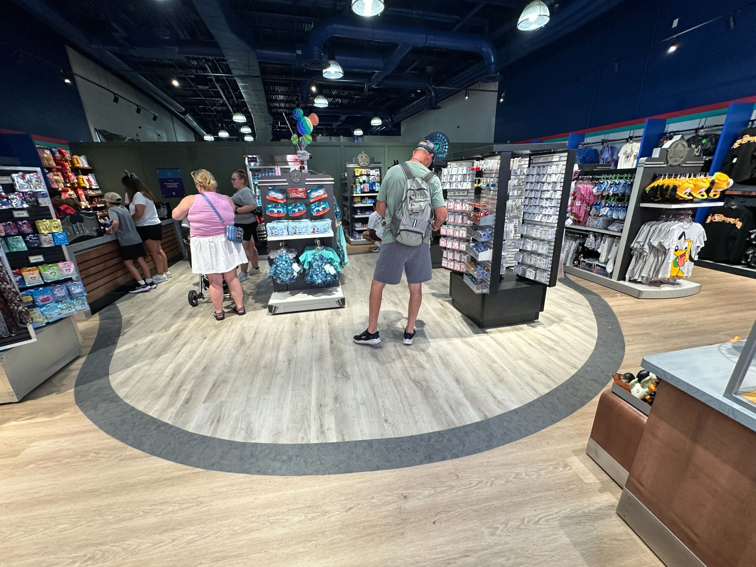 People browsing merchandise in a brightly lit gift shop with shelves of toys, shirts, and souvenirs.