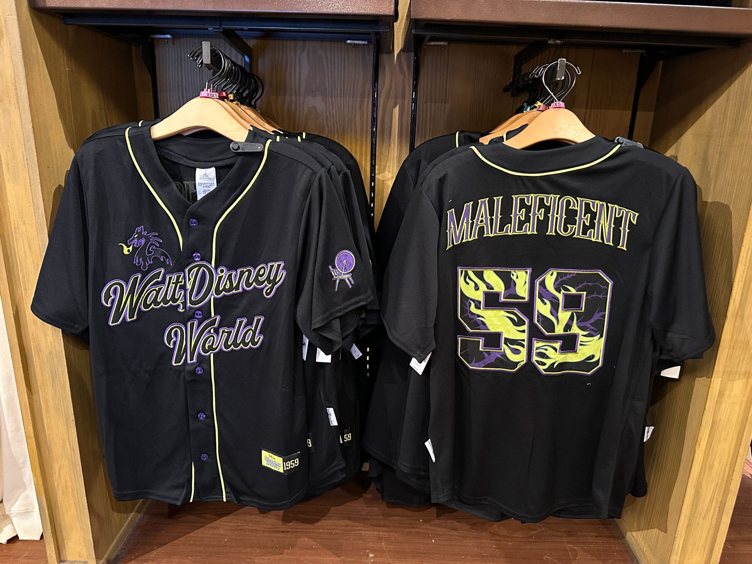 Two black baseball jerseys on hangers; front reads "Walt Disney World", back reads "Maleficent 59" in green and purple.