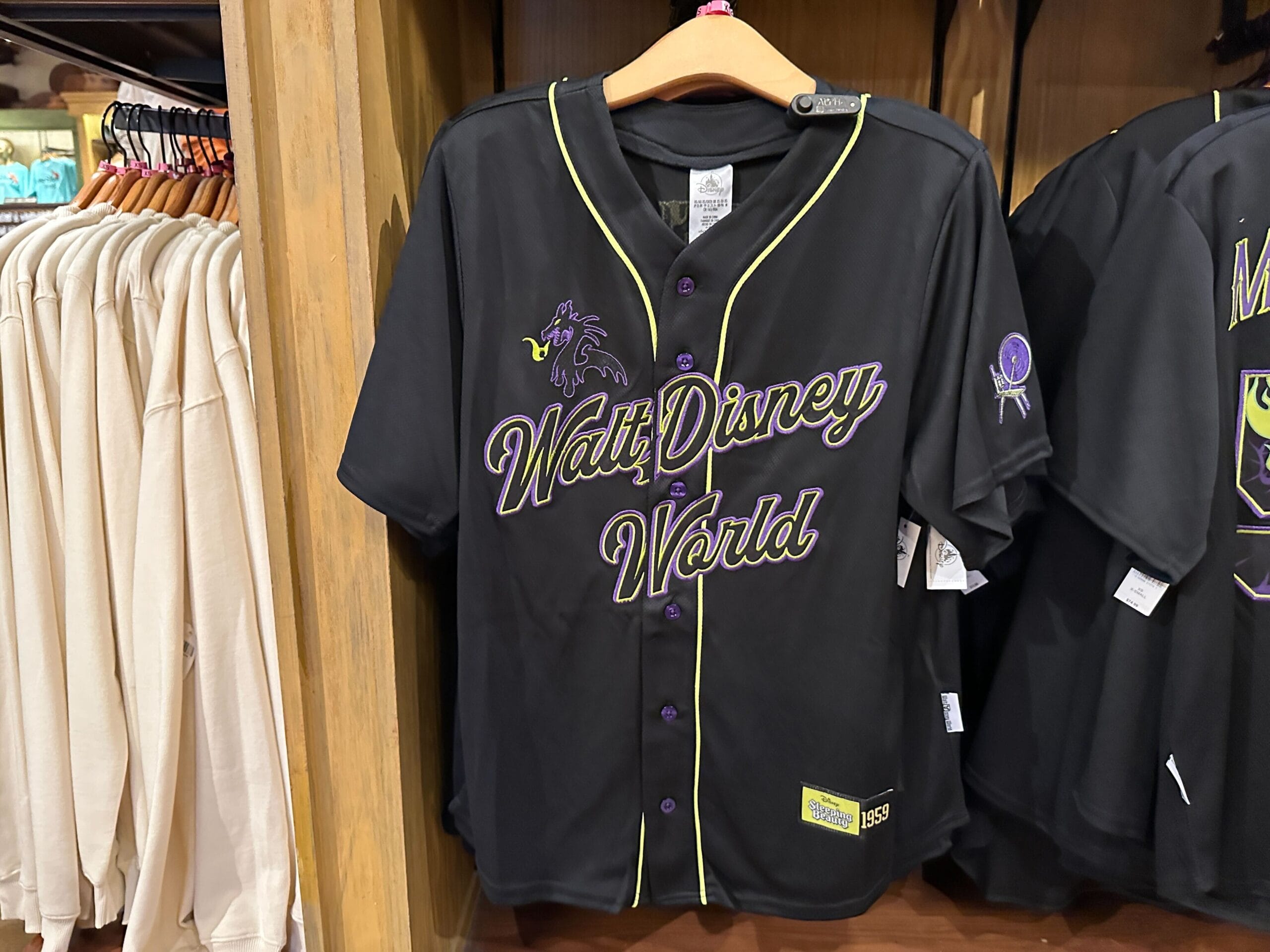 Black Walt Disney World baseball jersey with yellow trim and purple lettering, hanging on a rack in a store.