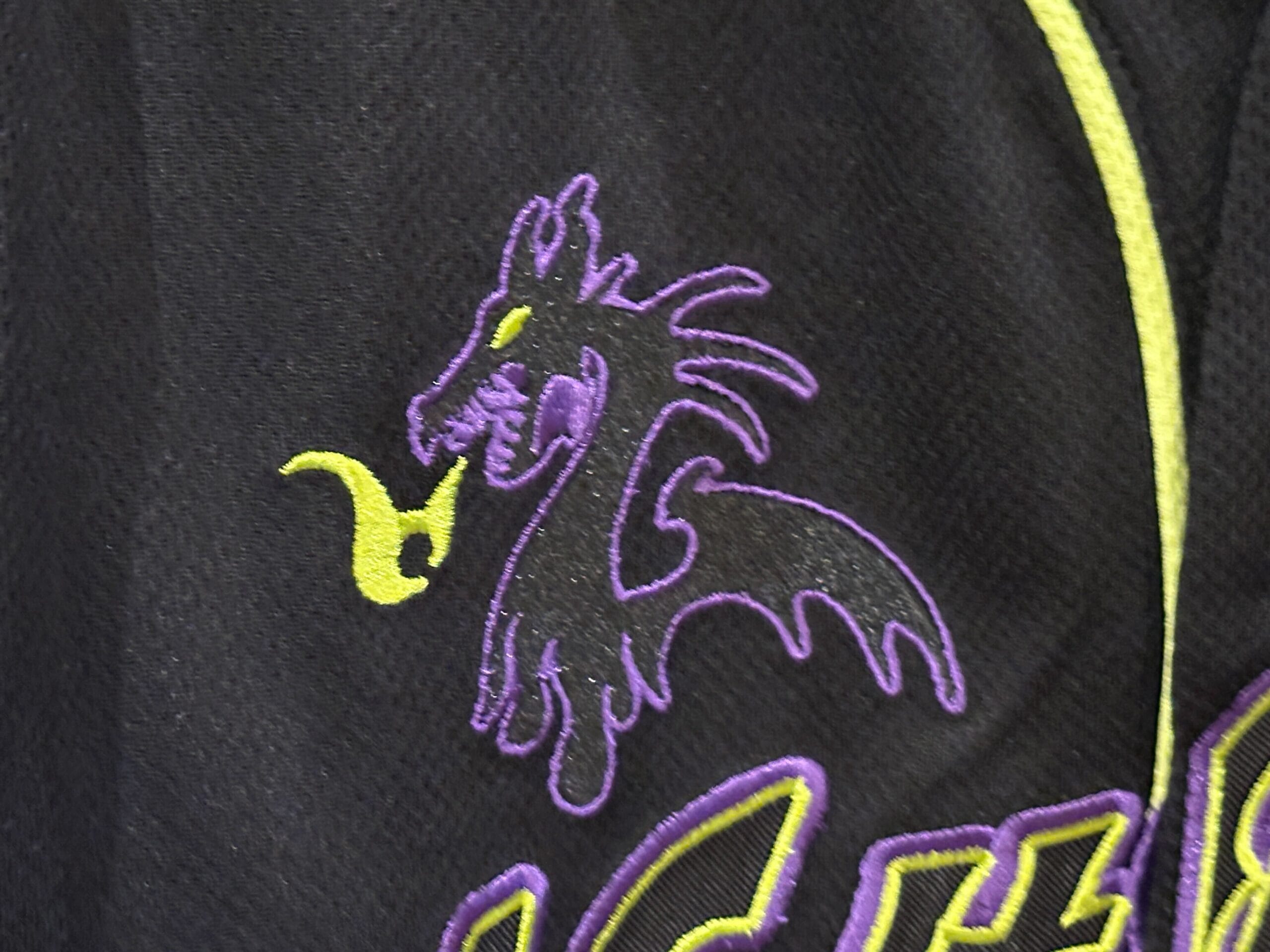 Purple dragon outline breathing yellow fire, embroidered on black fabric with yellow and purple accents.