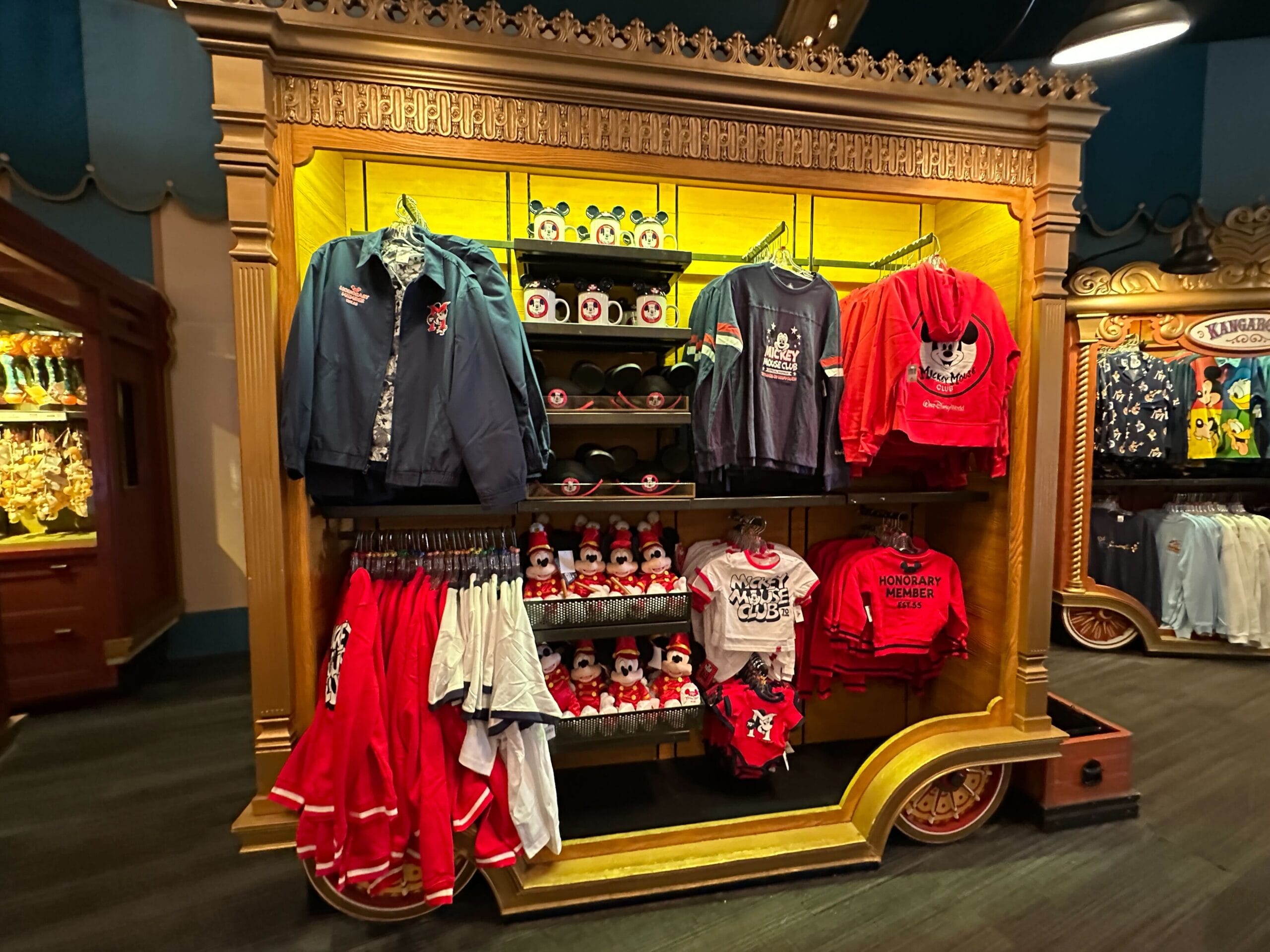 A display of Disney-themed clothing, hats, and plush toys on a golden cart in a store.