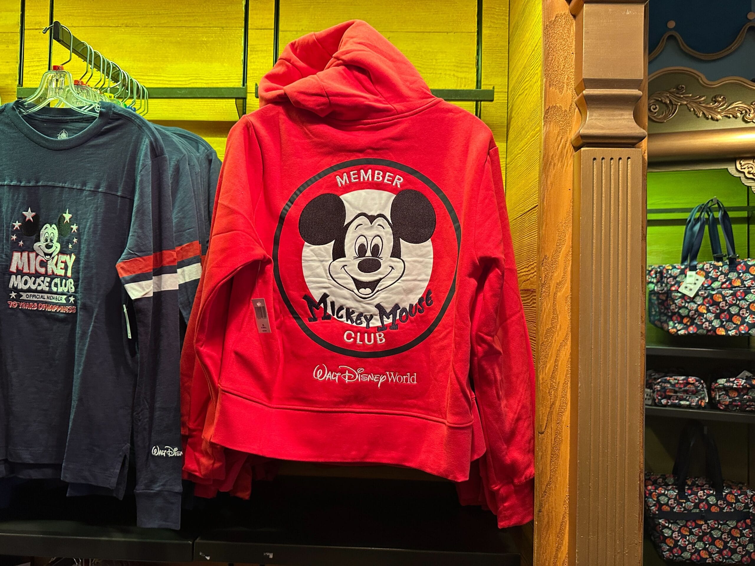 Red hoodie with Mickey Mouse Club logo and text "Member Mickey Mouse Club @ Walt Disney World" displayed in a store.