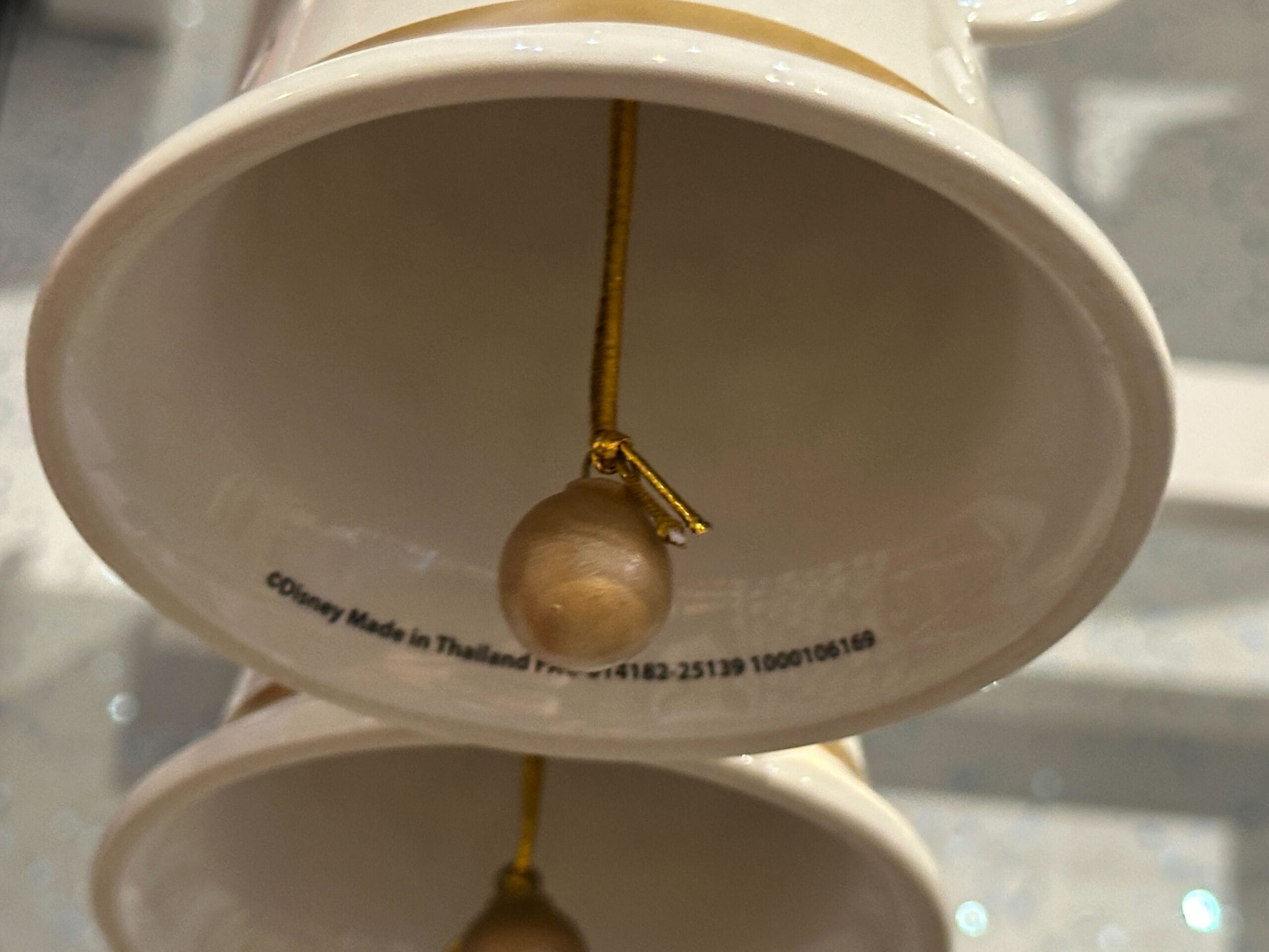 Close-up of the inside of two white ceramic bells with gold clappers and text printed inside the top bell.