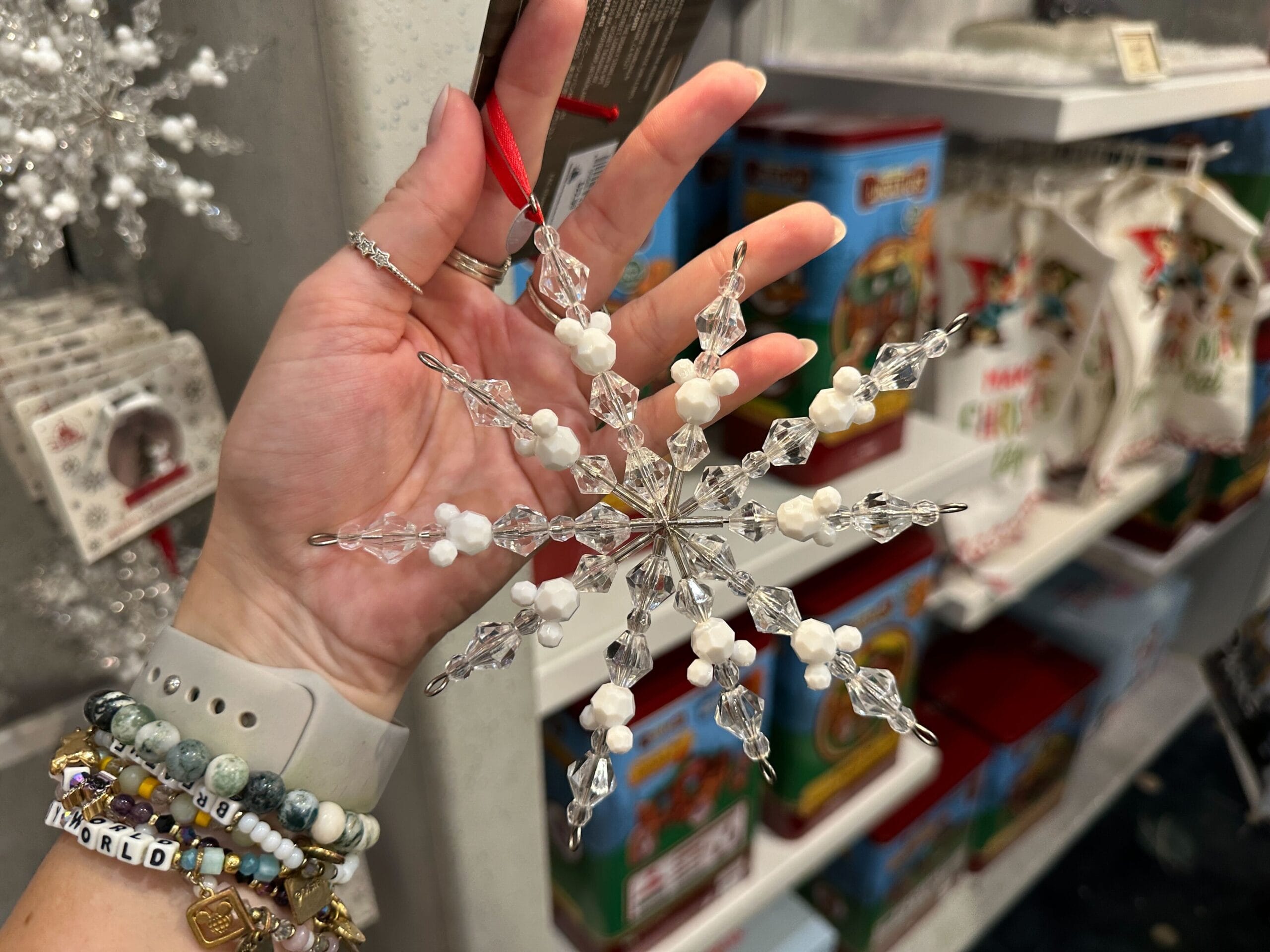 A hand holds a beaded snowflake ornament in a store filled with Christmas decorations and gifts.