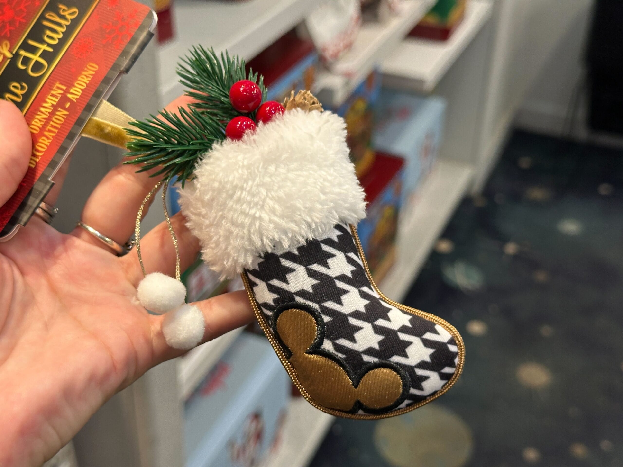 A hand holds a Christmas stocking ornament with a fluffy white cuff and black-and-white houndstooth pattern.