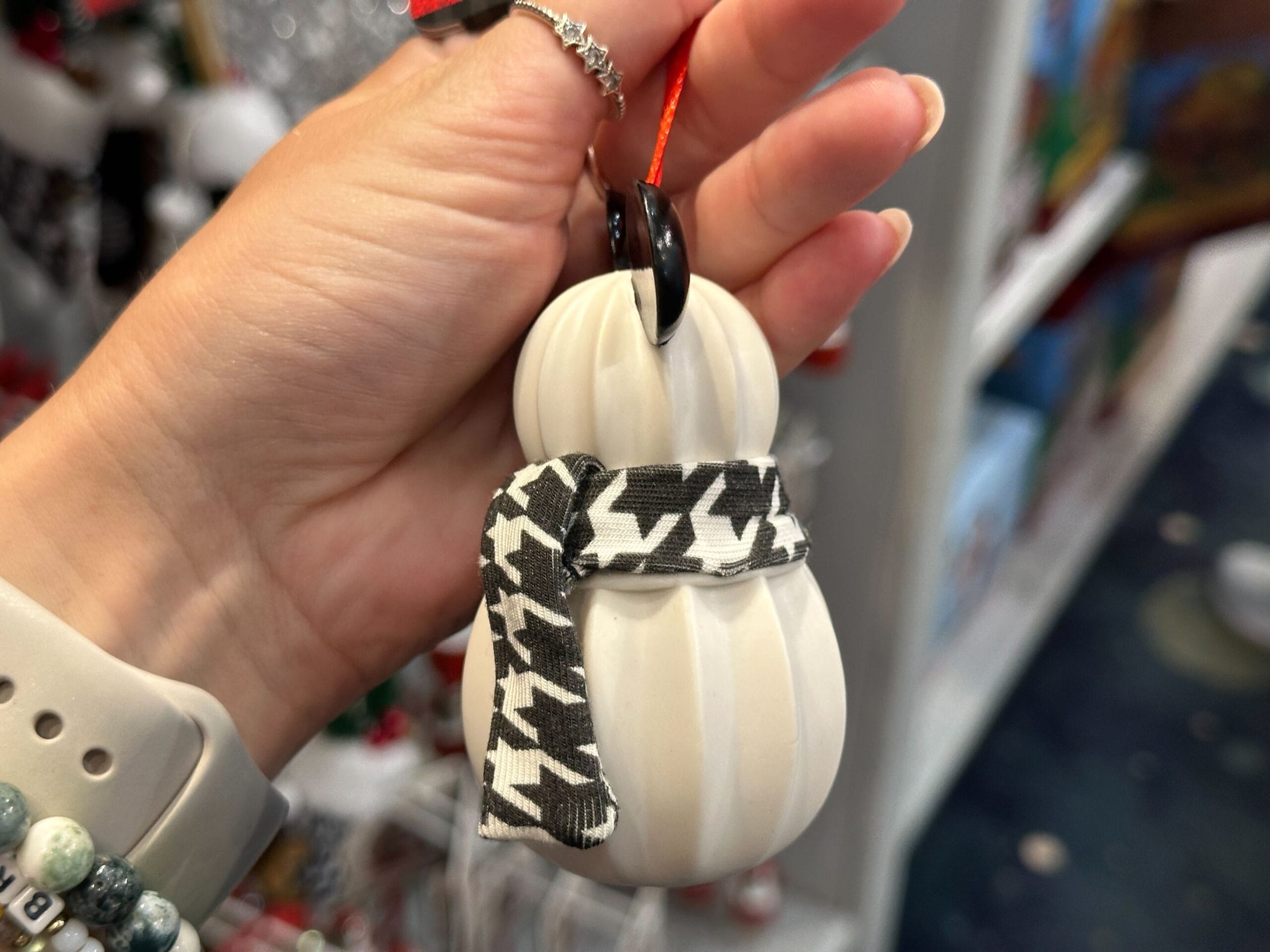 A hand holds a white pumpkin ornament with a black-and-white houndstooth scarf and a black stem.