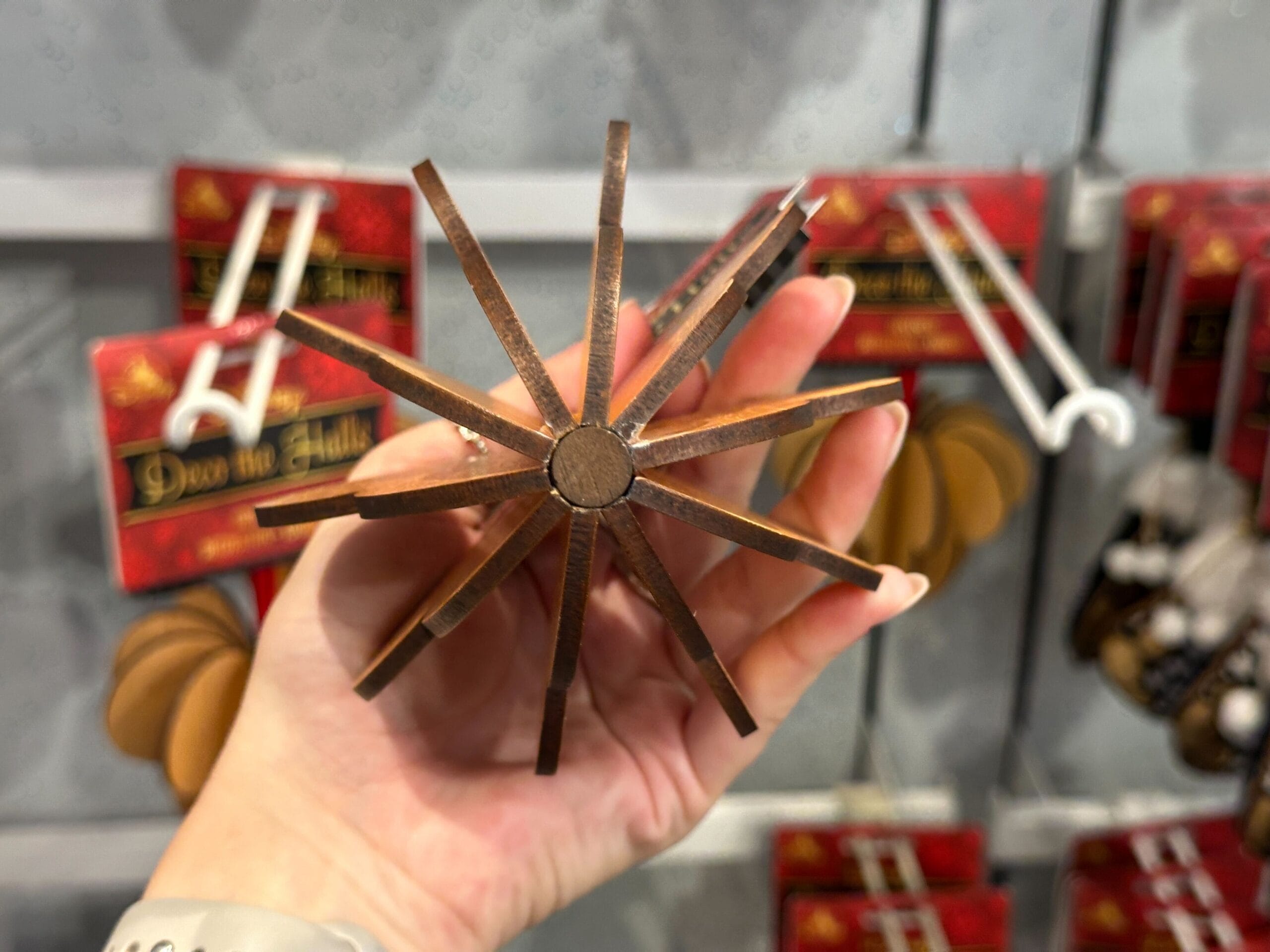 A hand holds a bronze star-shaped ornament in front of red holiday decorations on a store display.