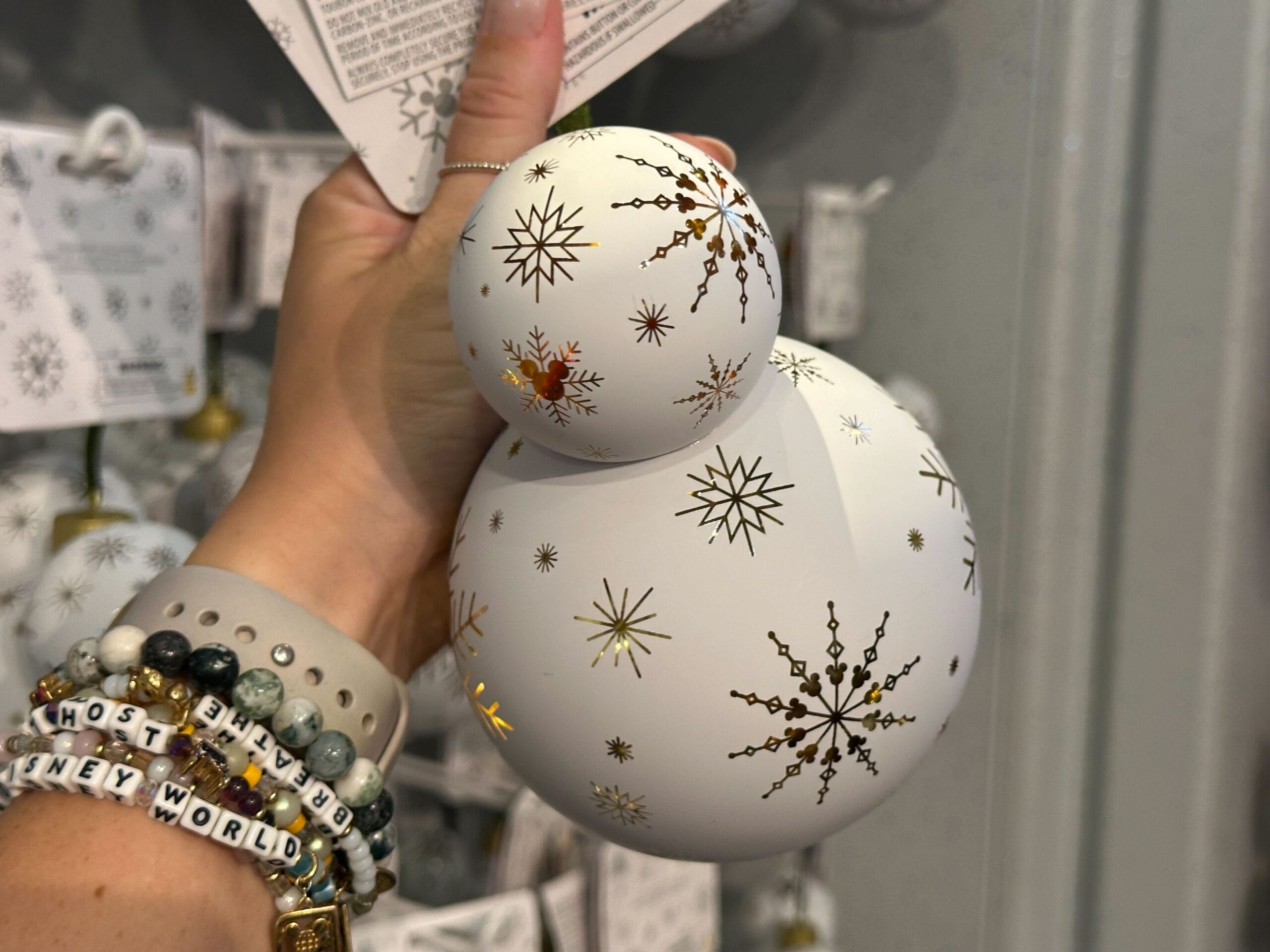 A hand holds a white snowman ornament decorated with gold and black snowflakes.