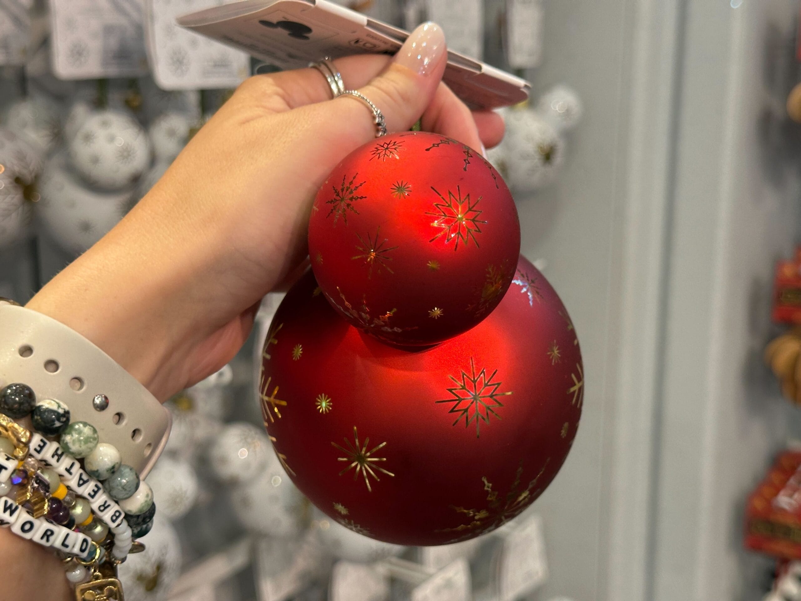 A hand holds a red, Mickey-shaped Christmas ornament with gold star patterns.