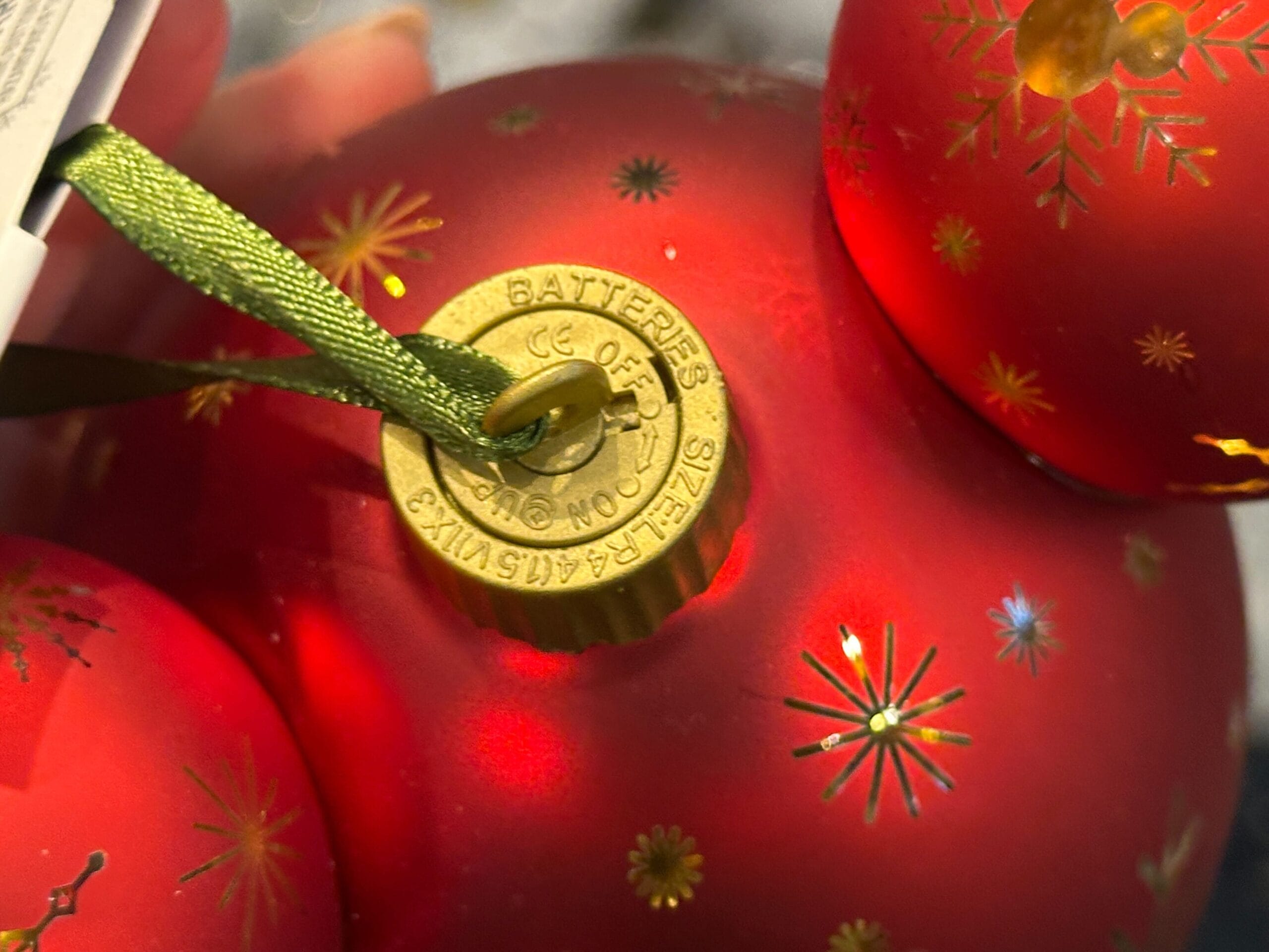 Close-up of a red Christmas ornament with gold starburst patterns and a gold cap holding a green hanging ribbon.