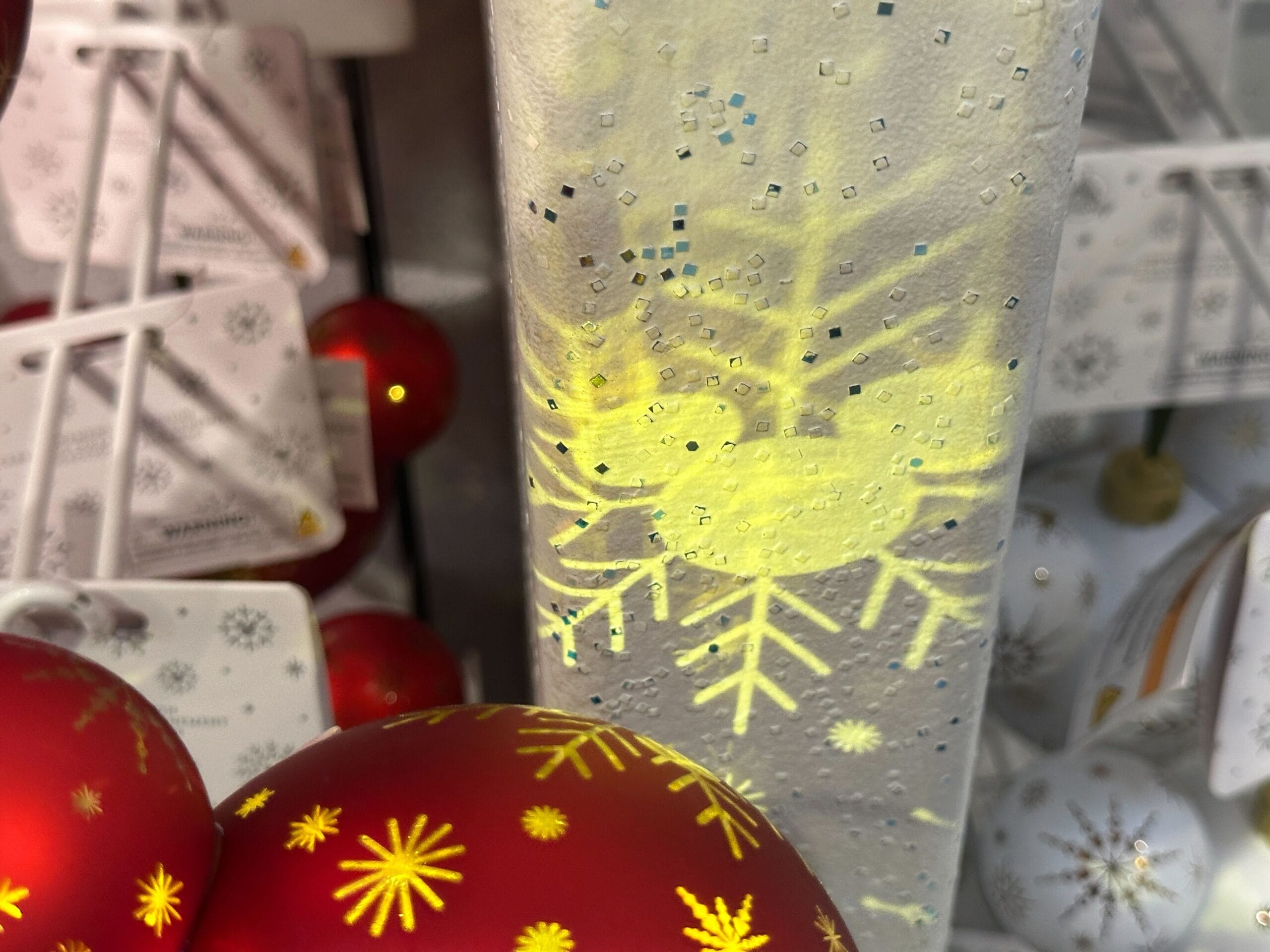 Close-up of Christmas ornaments with red and white balls and a glowing yellow snowflake design on frosted glass.