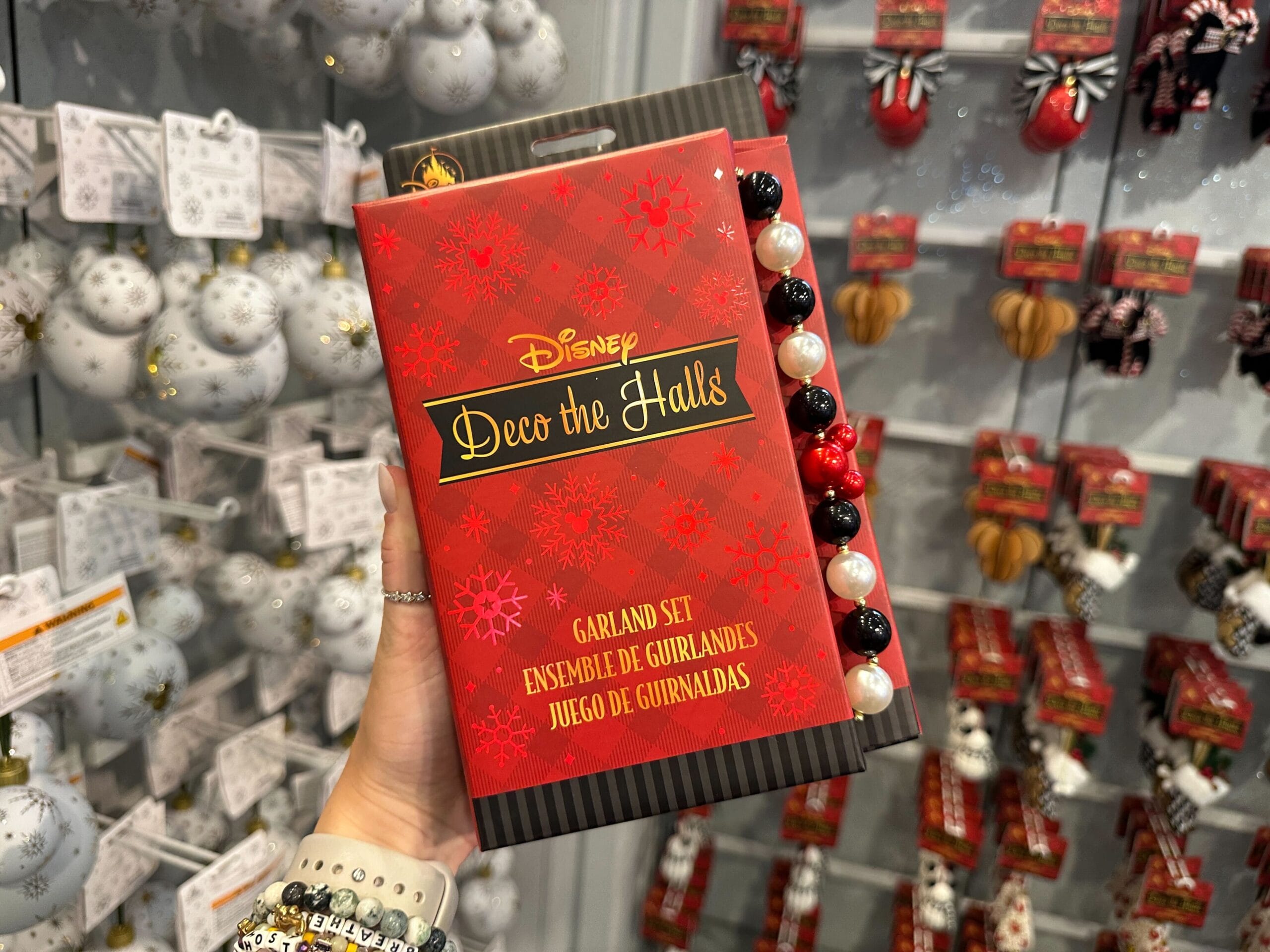 Hand holding a Disney "Deco the Halls" garland set in front of a display of Christmas ornaments.