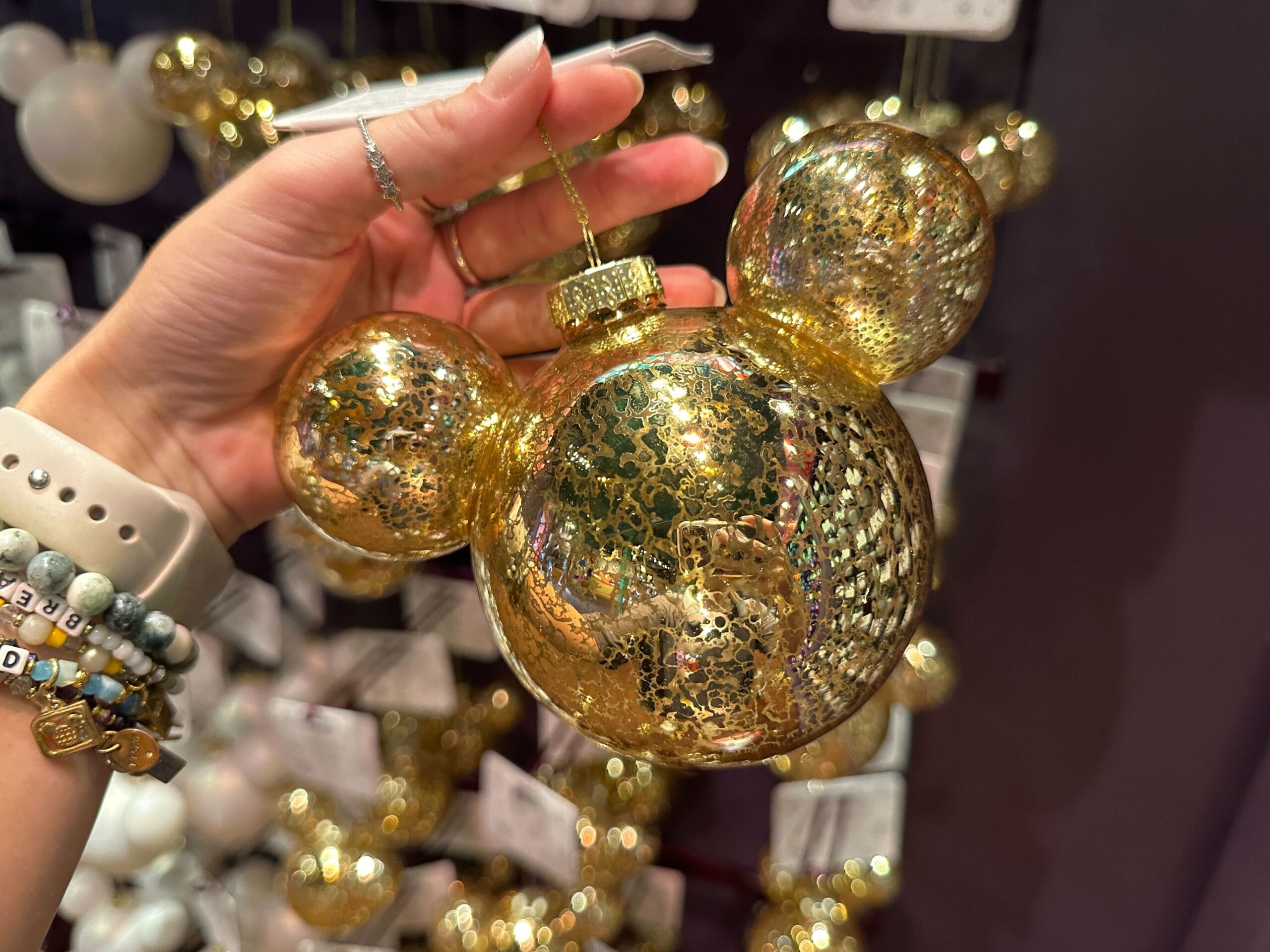 A hand holds a sparkling gold Mickey Mouse-shaped Christmas ornament in a store display.