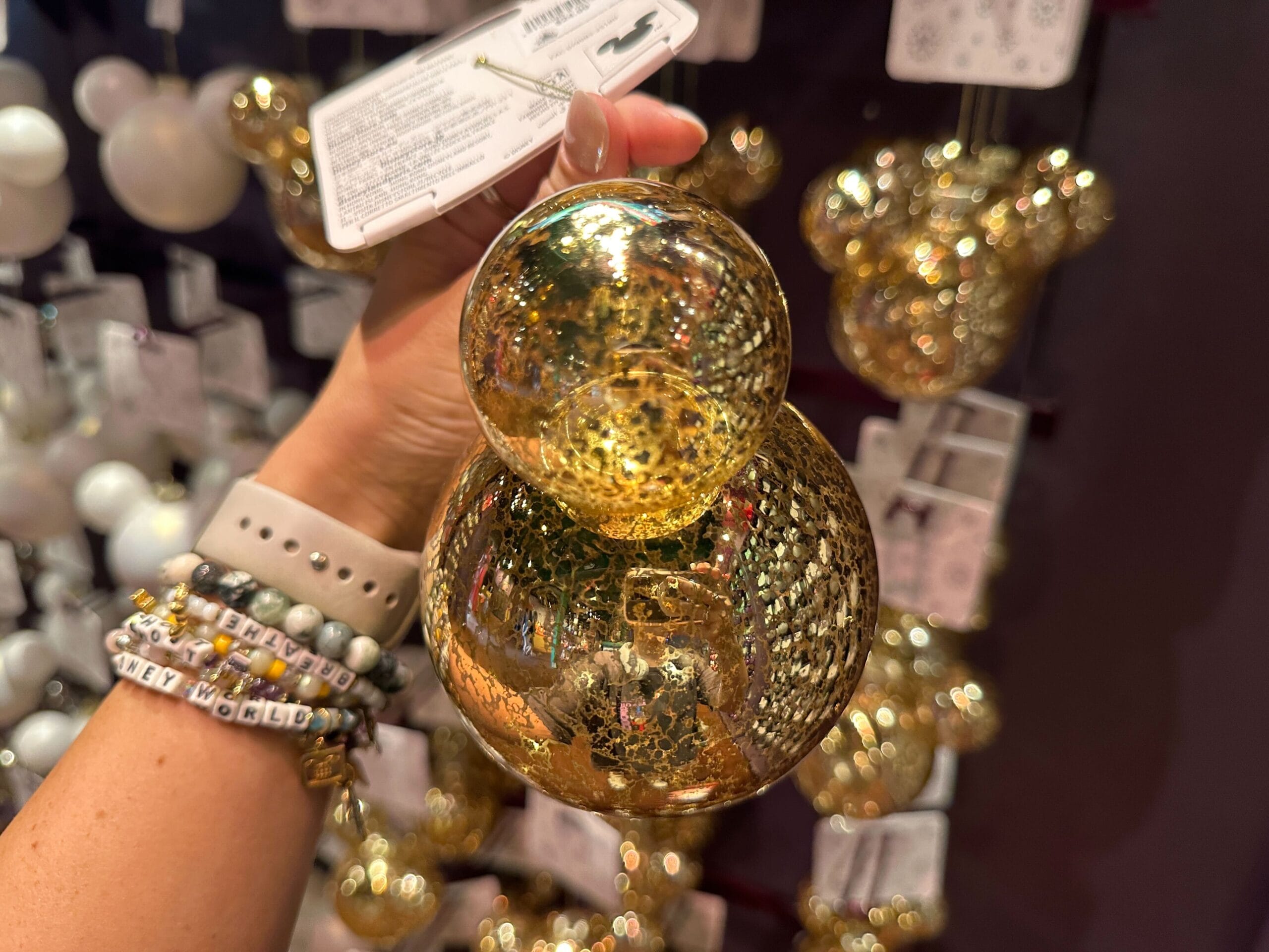 A hand holding a shiny gold Mickey Mouse-shaped ornament in a store display with more similar ornaments.