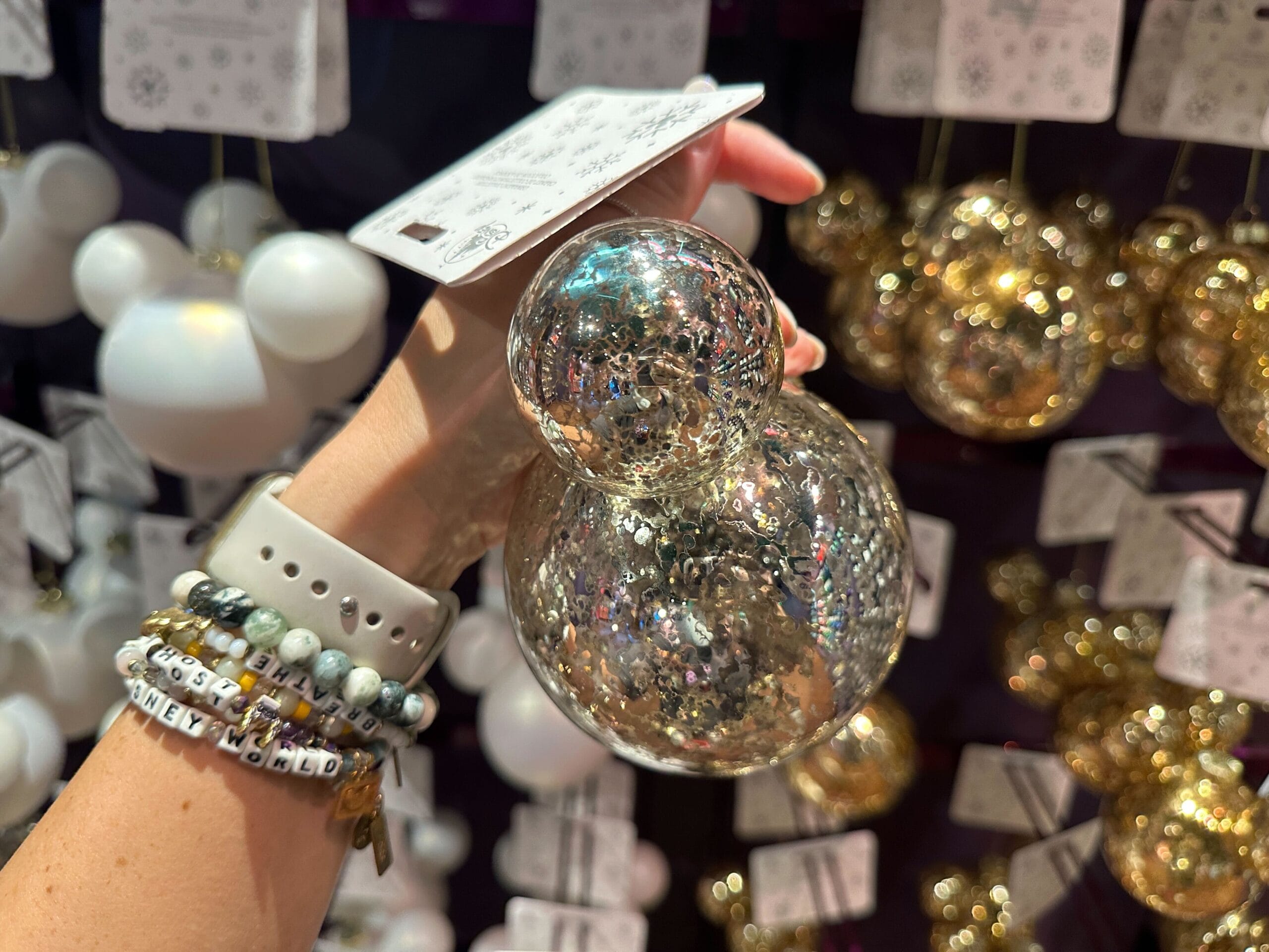 A hand holds a shiny, Mickey Mouse-shaped glass ornament among similar ornaments on display.