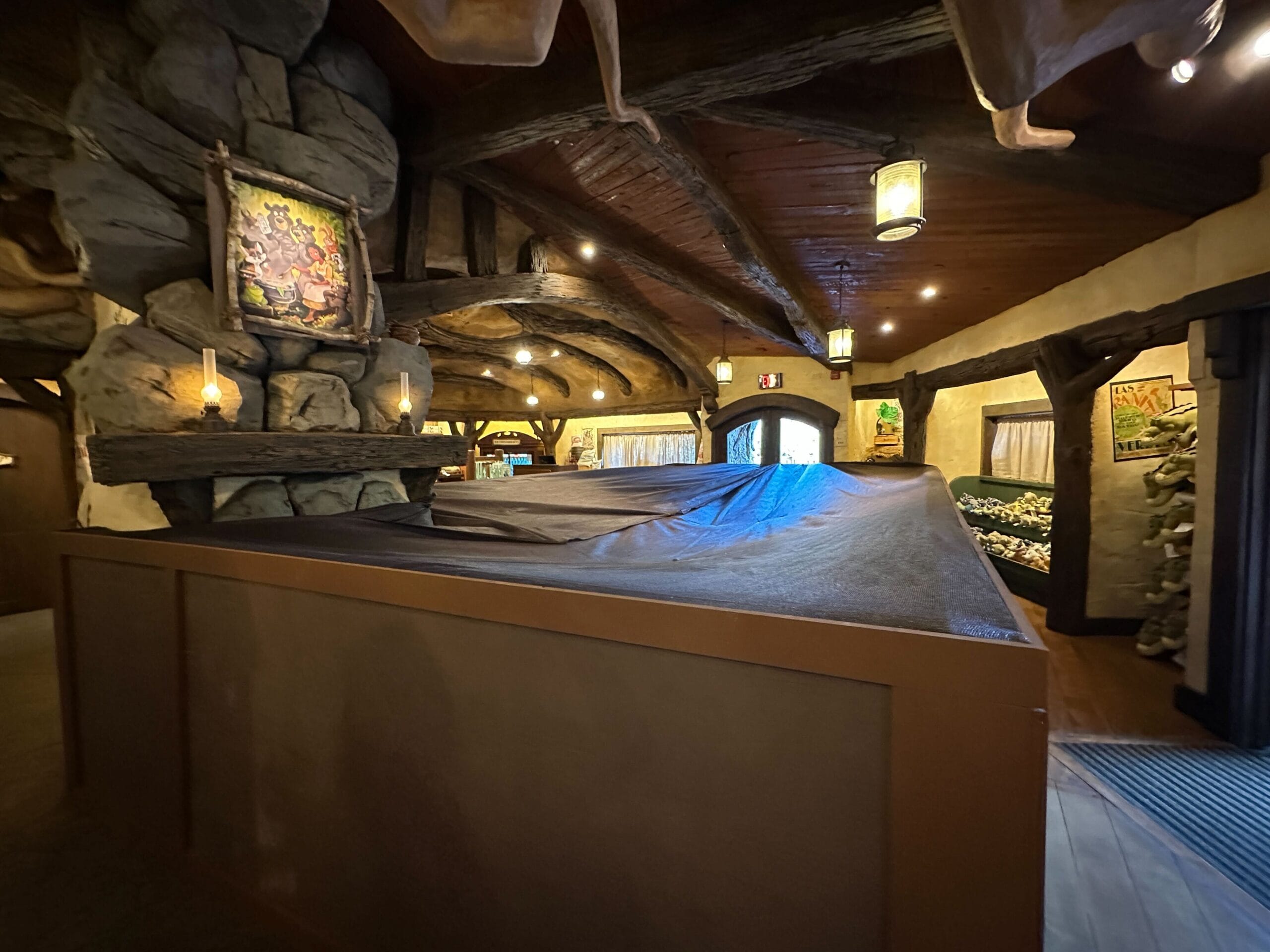 A rustic, wooden interior with stone walls and beams, art on the walls, and a covered structure in the center.