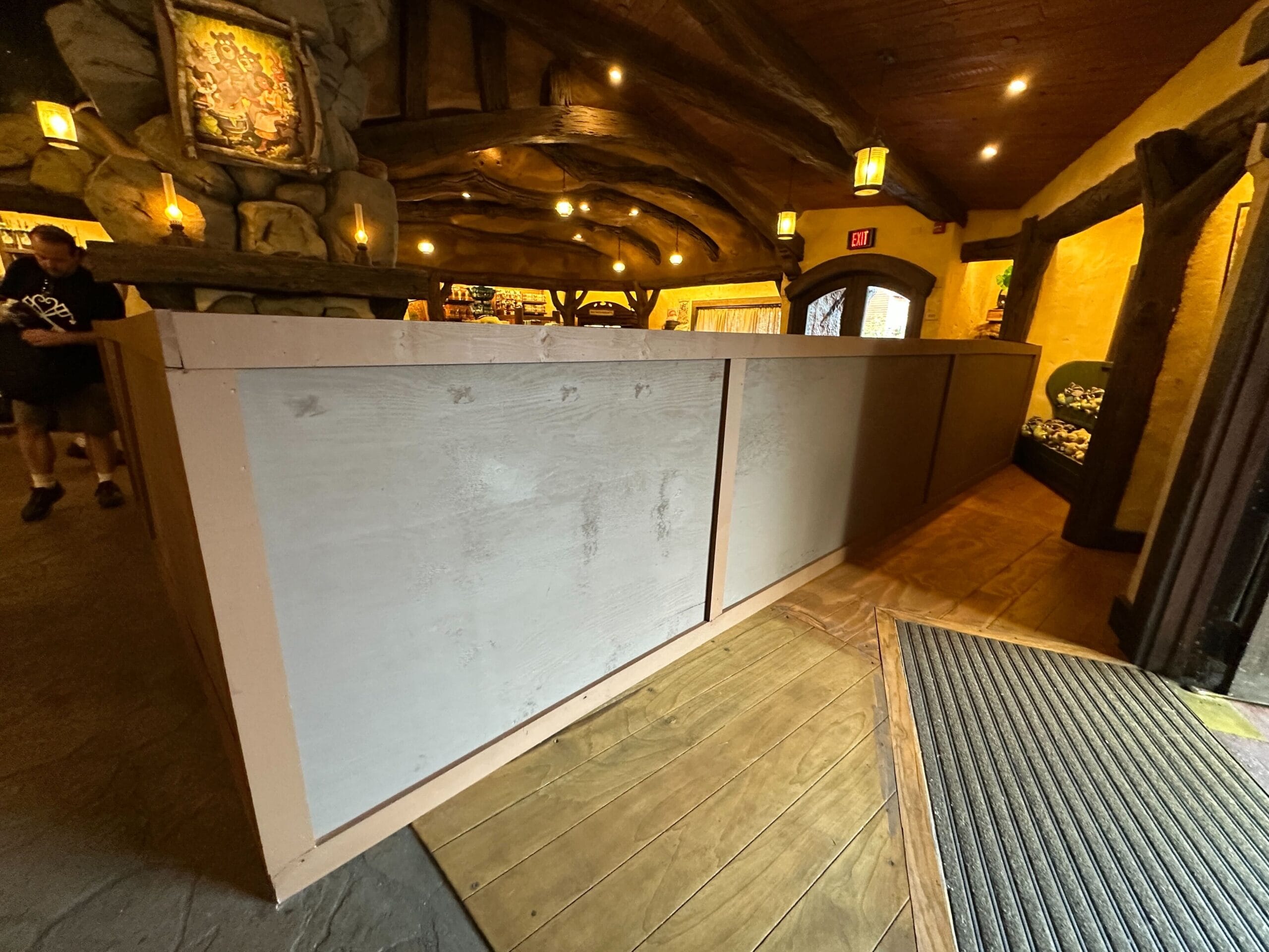 A wooden construction barrier blocks part of a rustic indoor walkway with warm lighting and wood accents.