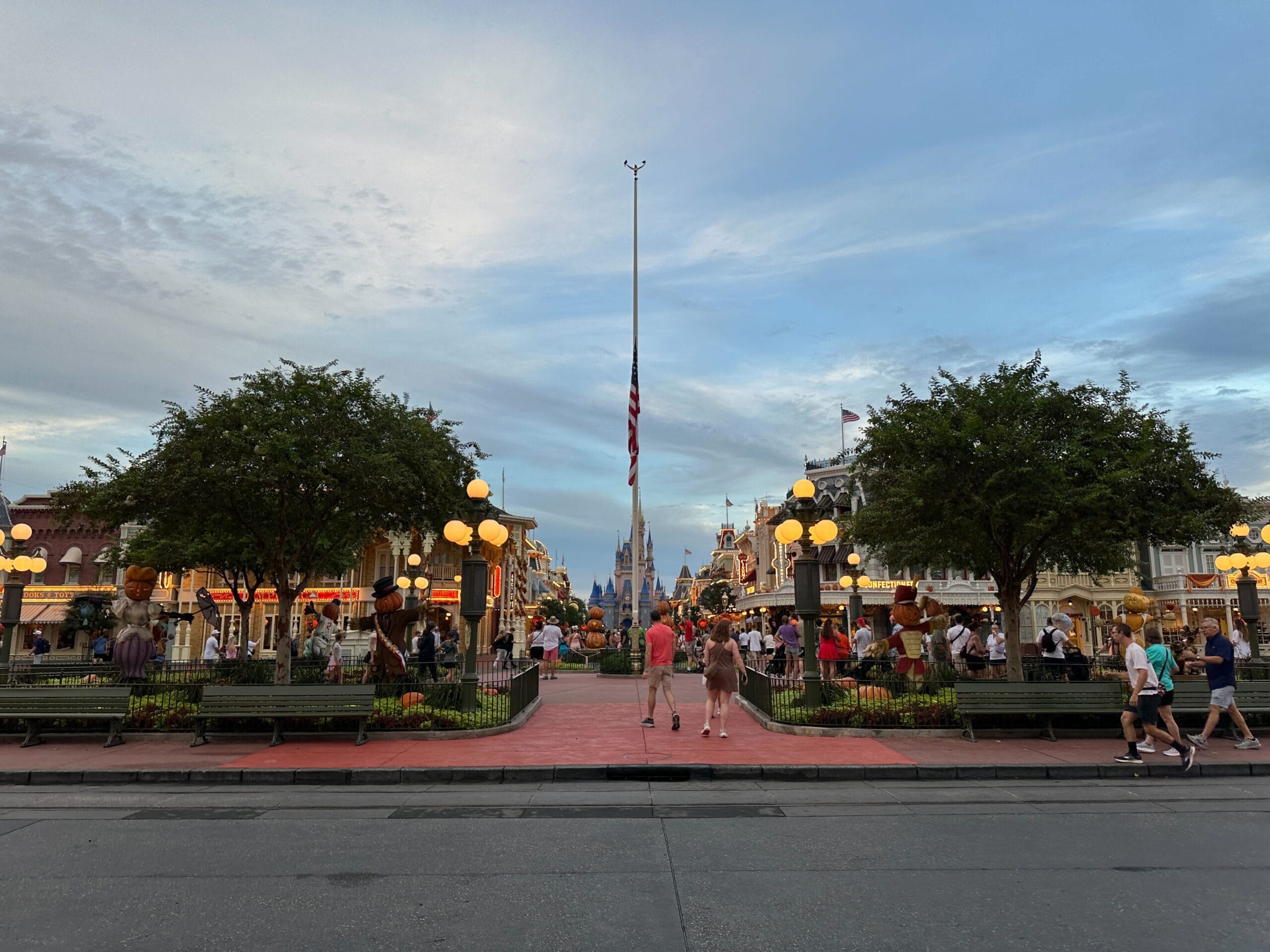 People walk along Main Street at Disney World, with an American flag at half-mast and Cinderella Castle in the background.
