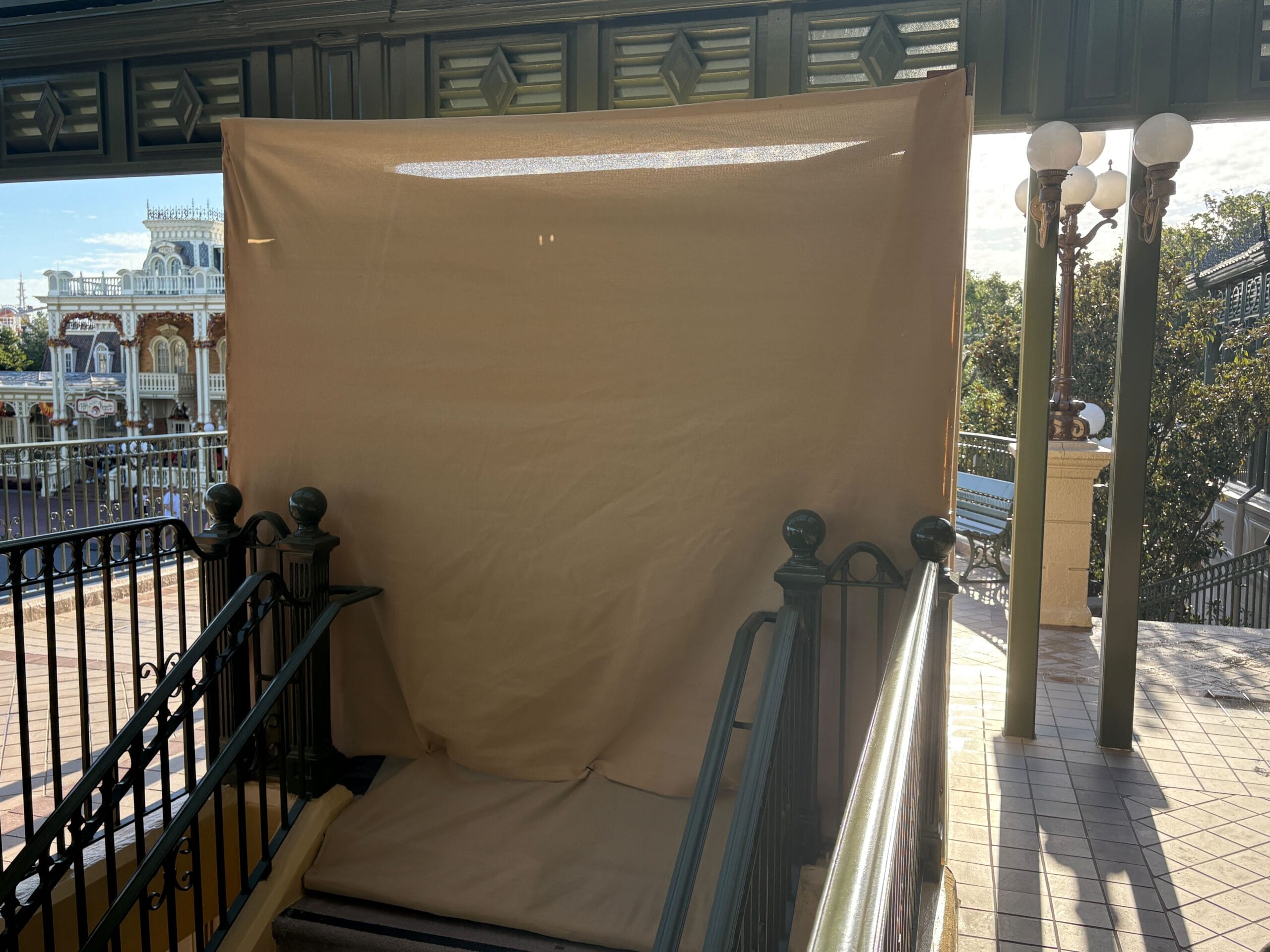 A staircase is blocked by a large beige tarp at an outdoor location with lamps and railings.