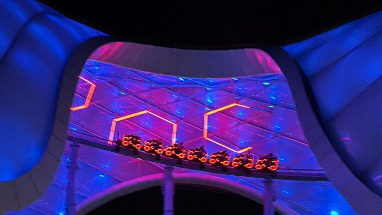A TRON Nighttime Overlay with a futuristic, blue-lit canopy at Magic Kingdom and people strolling below.