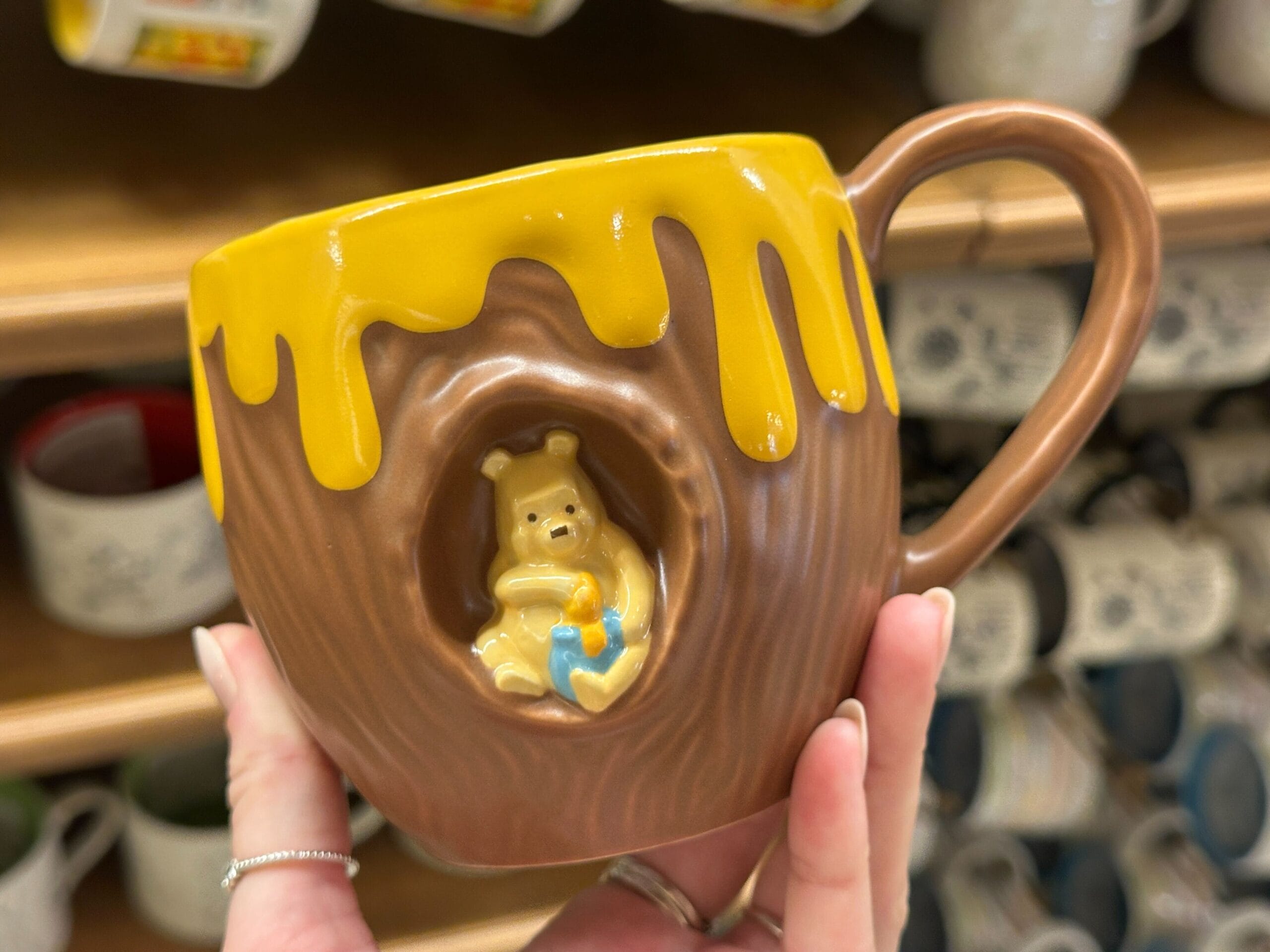 A mug shaped like a tree trunk with yellow drips and a bear holding a blue pot inside a hollow.