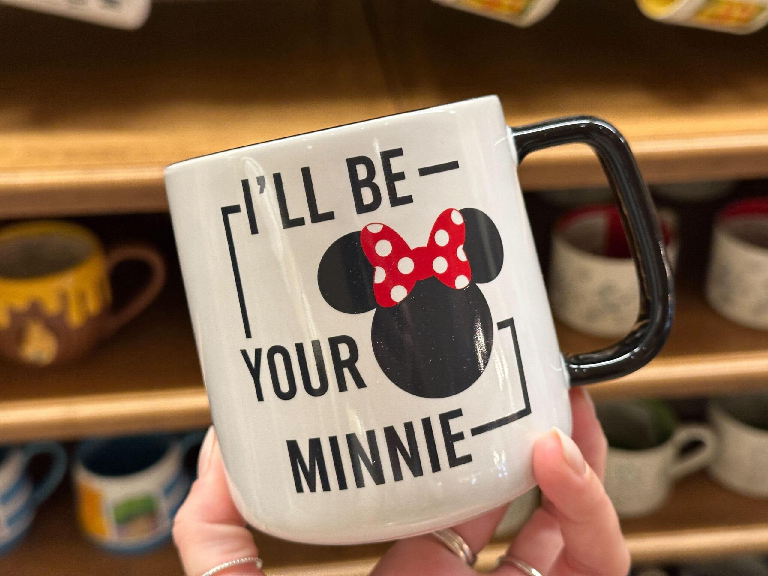 A hand holds a mug with a Minnie Mouse graphic and the text "I'll be your Minnie.