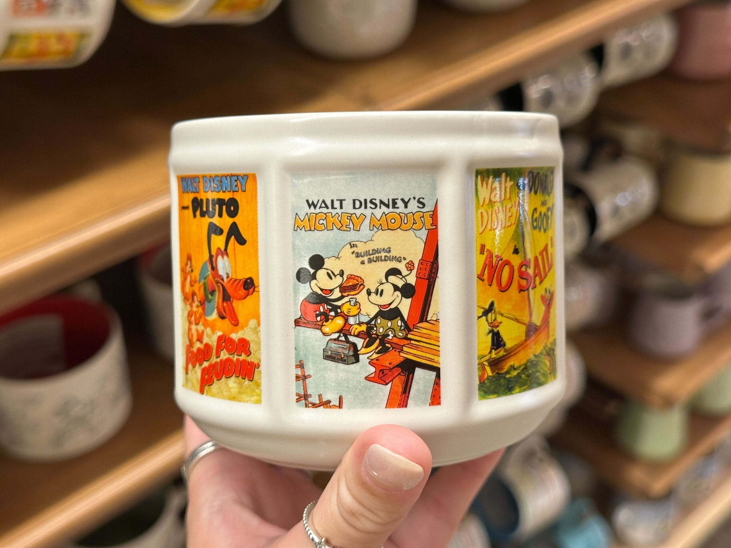 A hand holds a ceramic bowl adorned with vintage-style Disney posters of Mickey, Minnie, and Pluto.