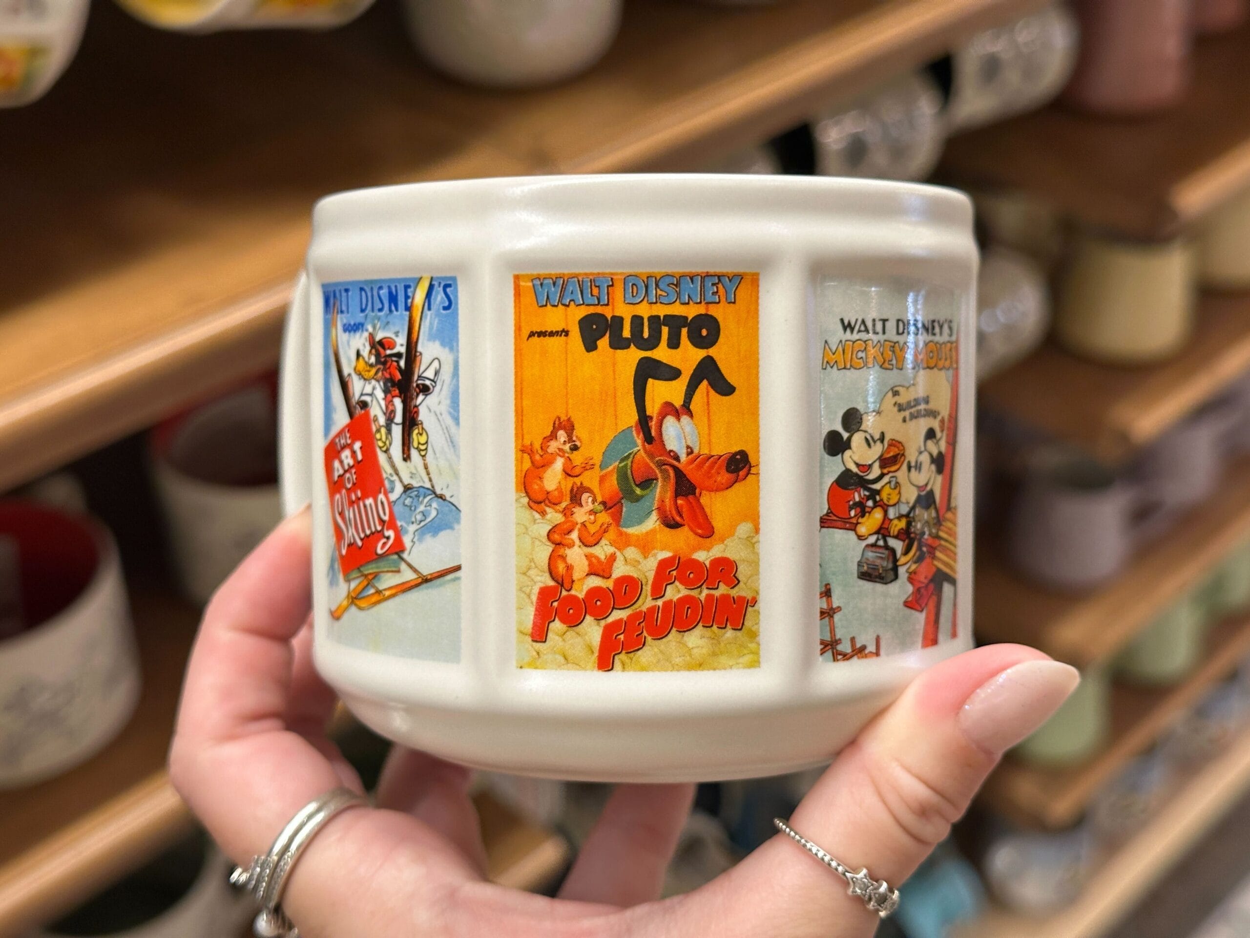 A hand holds a ceramic mug featuring vintage Walt Disney cartoon posters, including Mickey Mouse and Minnie.