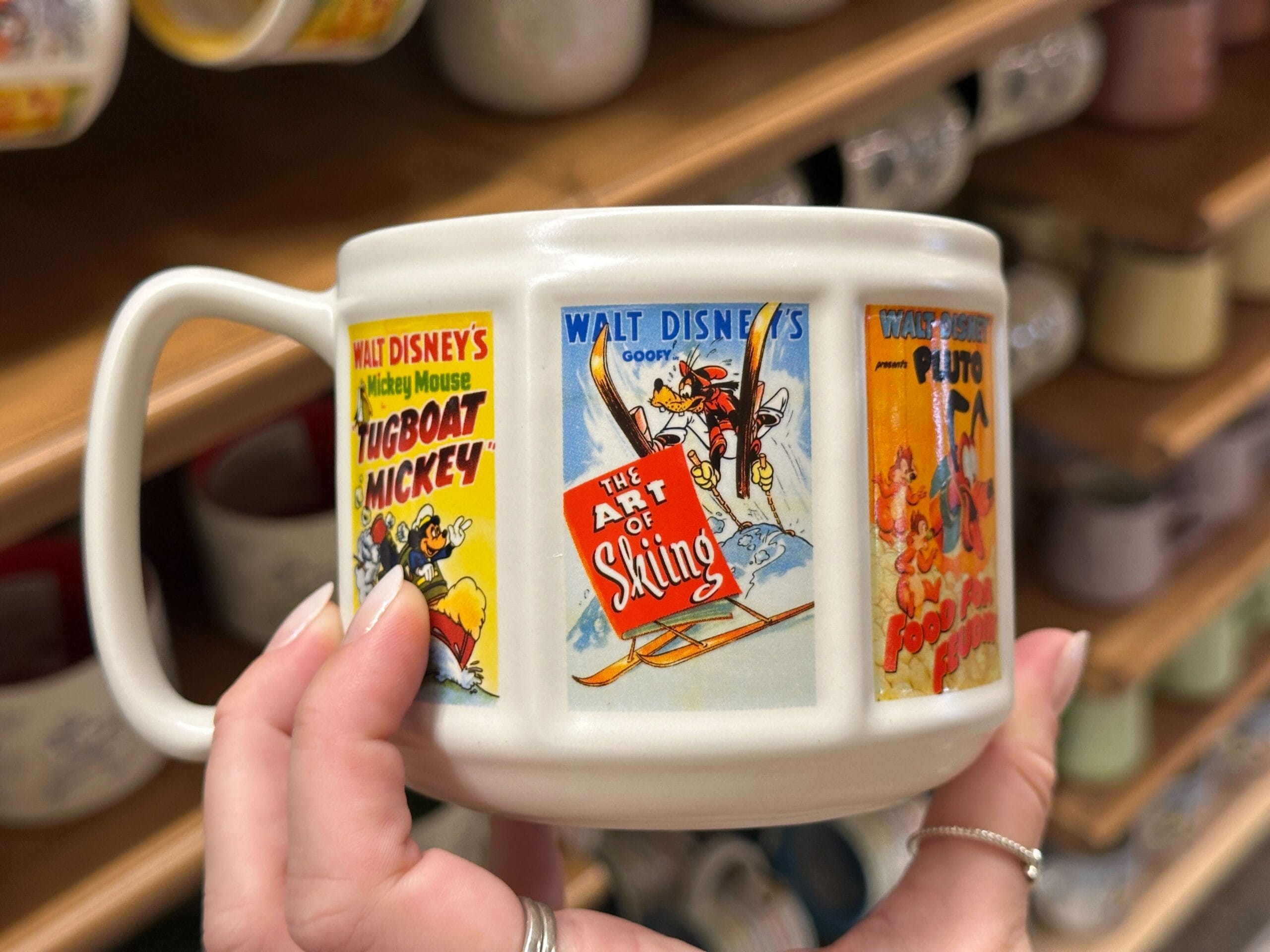 Hand holding a mug with vintage Walt Disney cartoon posters of Mickey, Minnie, Goofy, Pluto, and Winnie the Pooh.