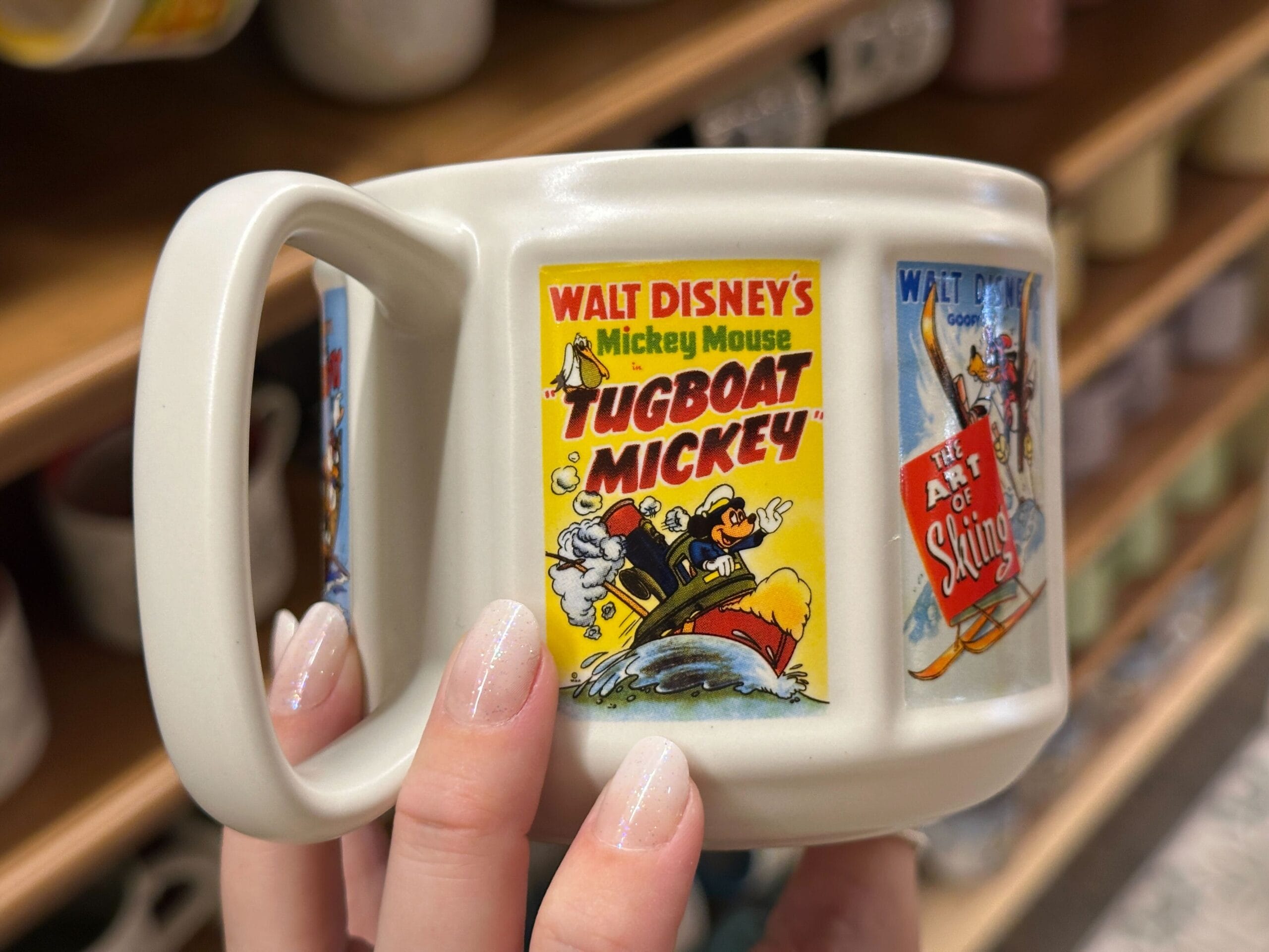 A hand holds a mug featuring a vintage "Tugboat Mickey" comic-style illustration with Mickey and Minnie.
