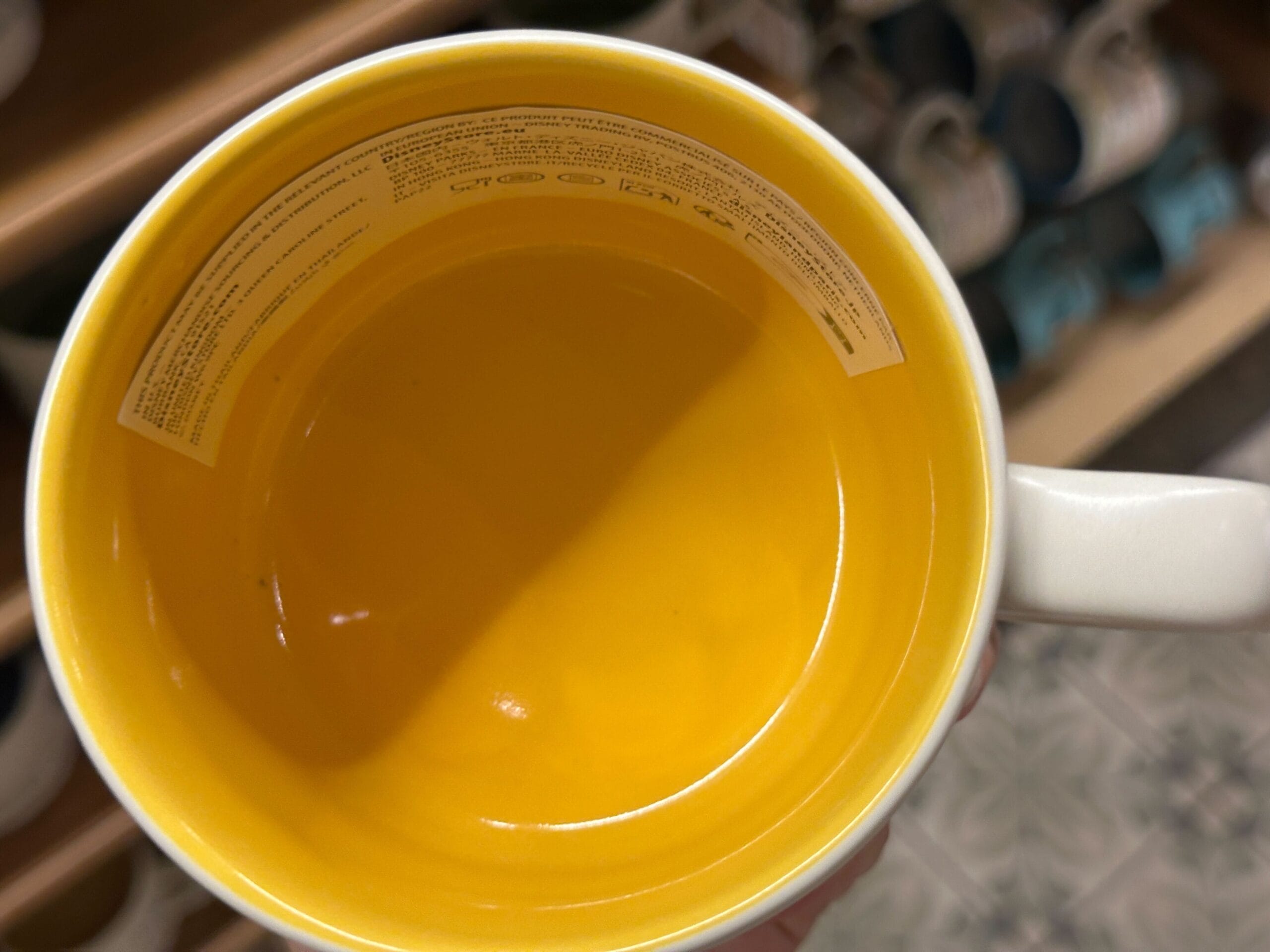 Top view of a yellow mug with a white rim, featuring a Winnie the Pooh label, held above a patterned floor.