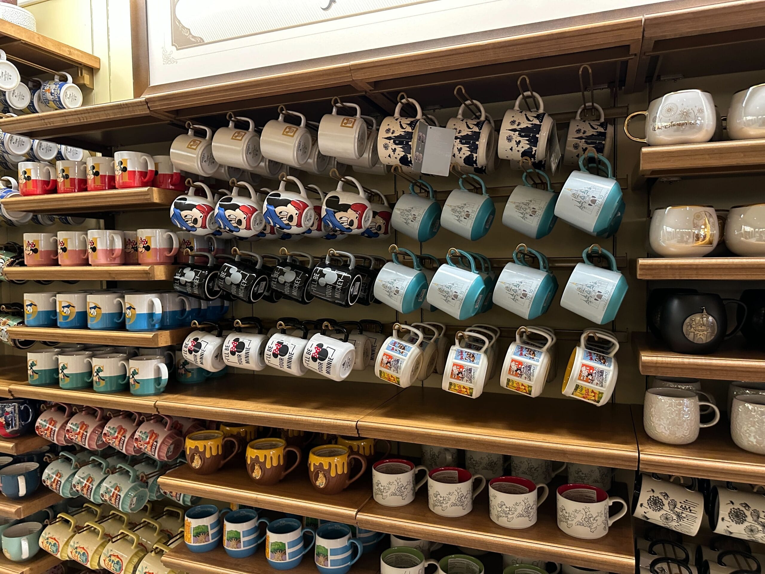 Shelves filled with colorful mugs, including Mickey and Winnie the Pooh designs, neatly hanging by their handles in rows.