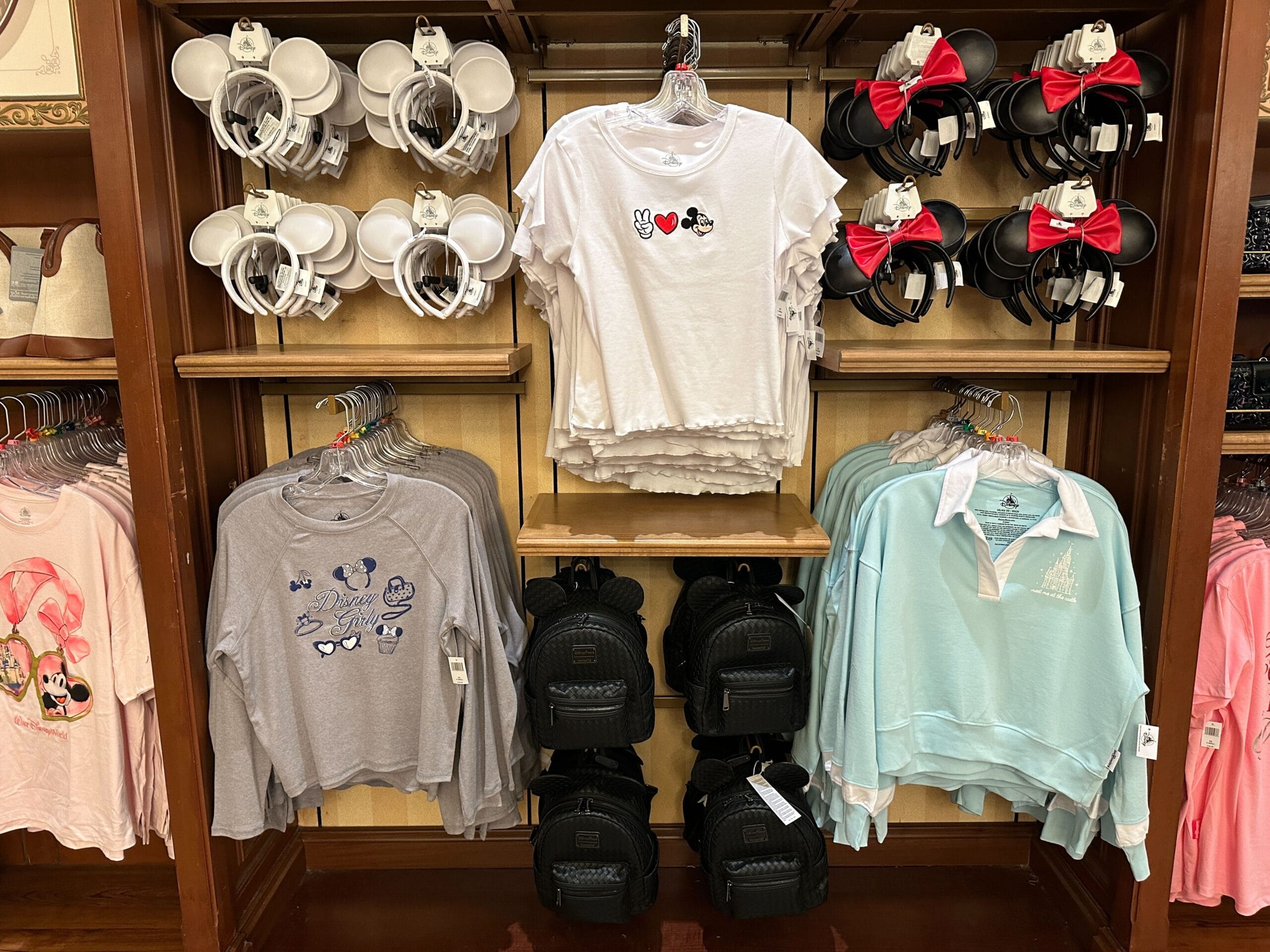 Disney-themed shirts, mugs, and Minnie Mouse ear headbands displayed on a wooden store shelf.