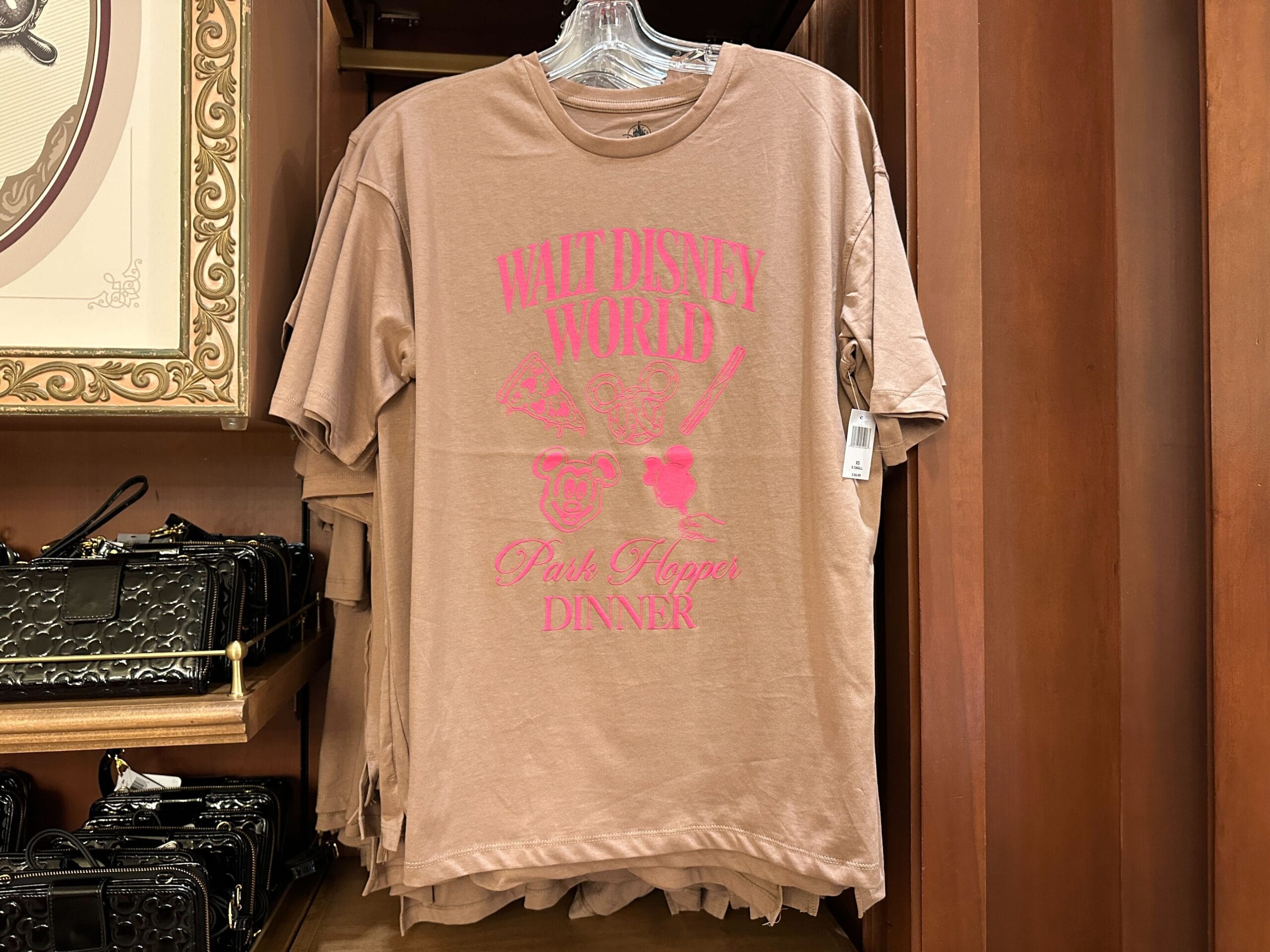 Tan t-shirt with neon pink "Walt Disney World Pink Hopper Dinner" text and graphics, hanging on a store rack.