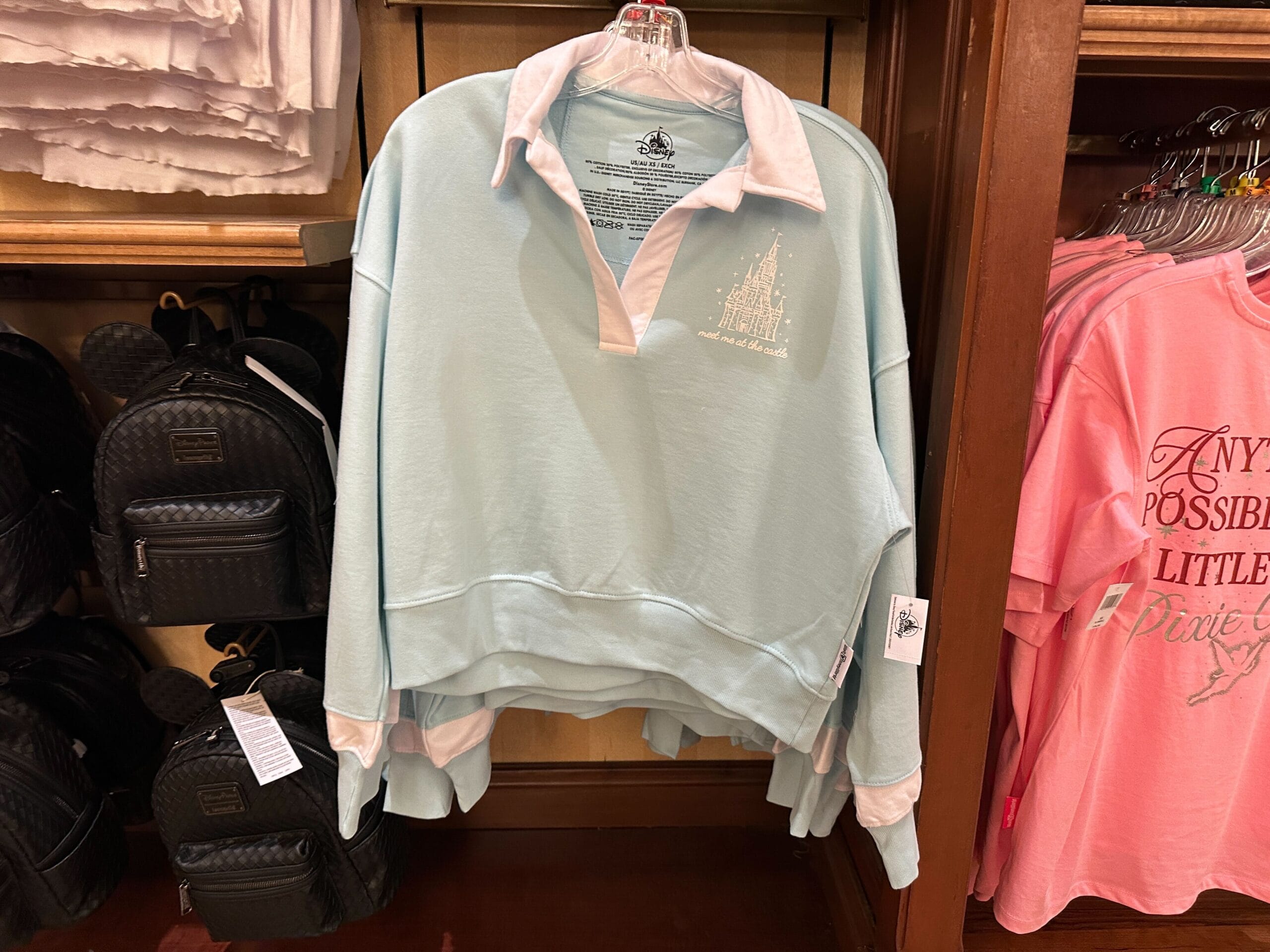 Light blue pullover with white collar and cuffs, featuring a white castle graphic, displayed on a store rack.