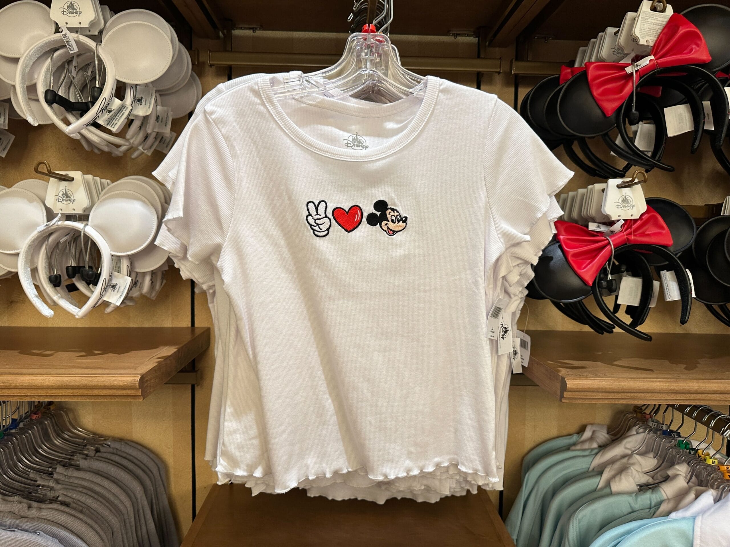 White t-shirt with peace sign, heart, and Mickey Mouse face symbols, displayed among Mickey Mouse ear headbands.