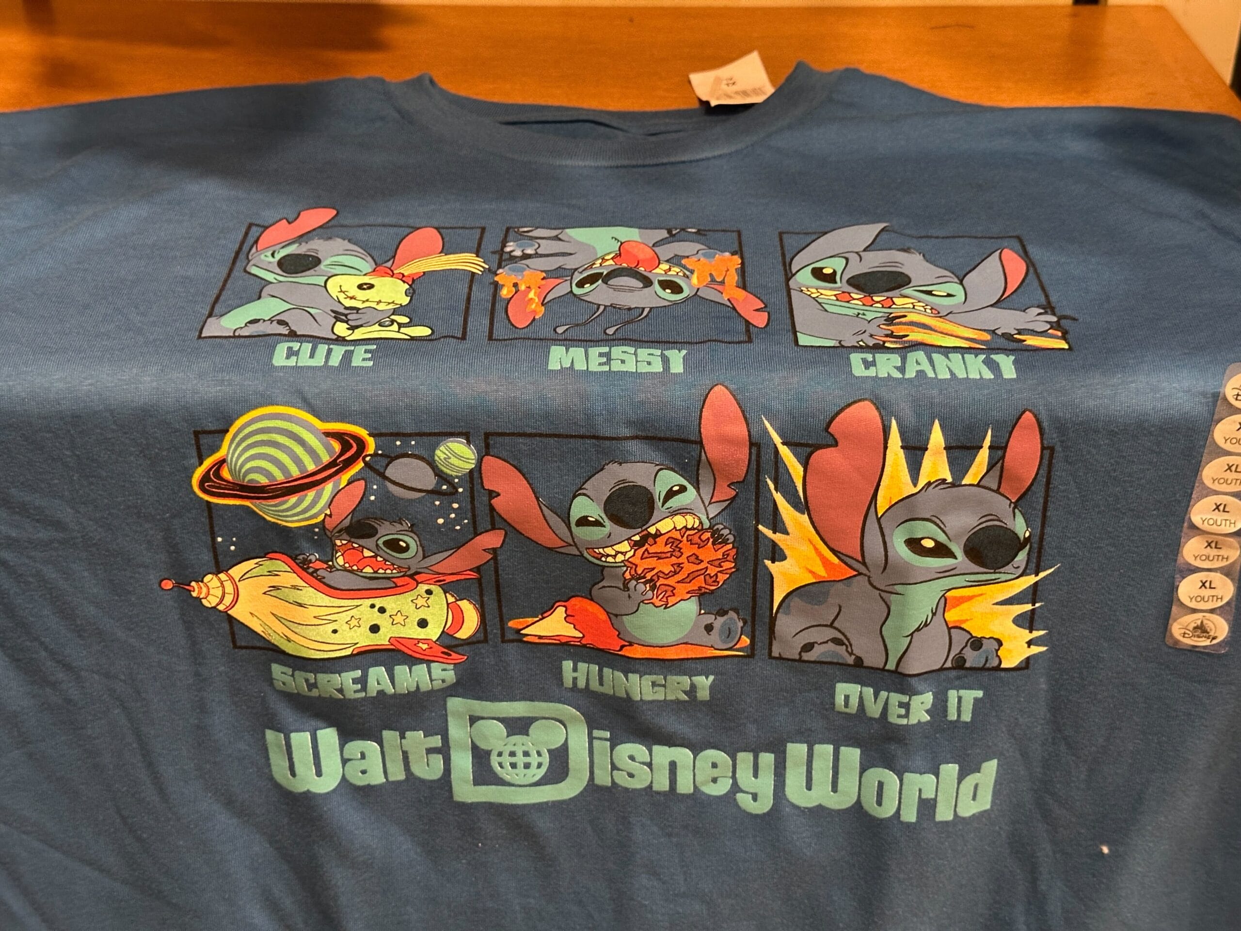 Blue T-shirt with six cartoon Stitch panels labeled: Cute, Messy, Cranky, Screams, Hungry, Over It. Walt Disney World text.