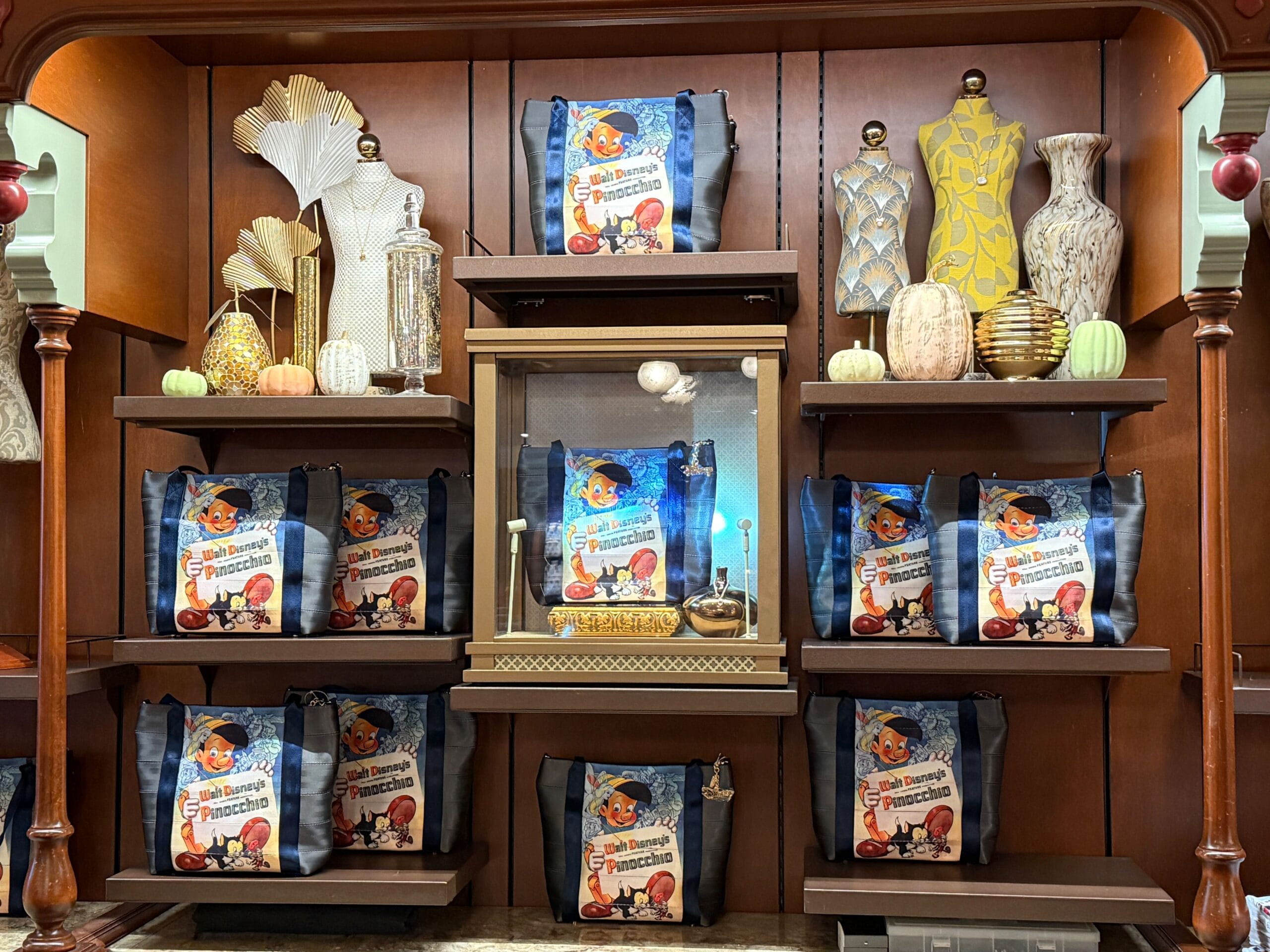 Shelves display decorative vases, pumpkins, and blue Pinocchio-themed tote bags in a wooden cabinet.