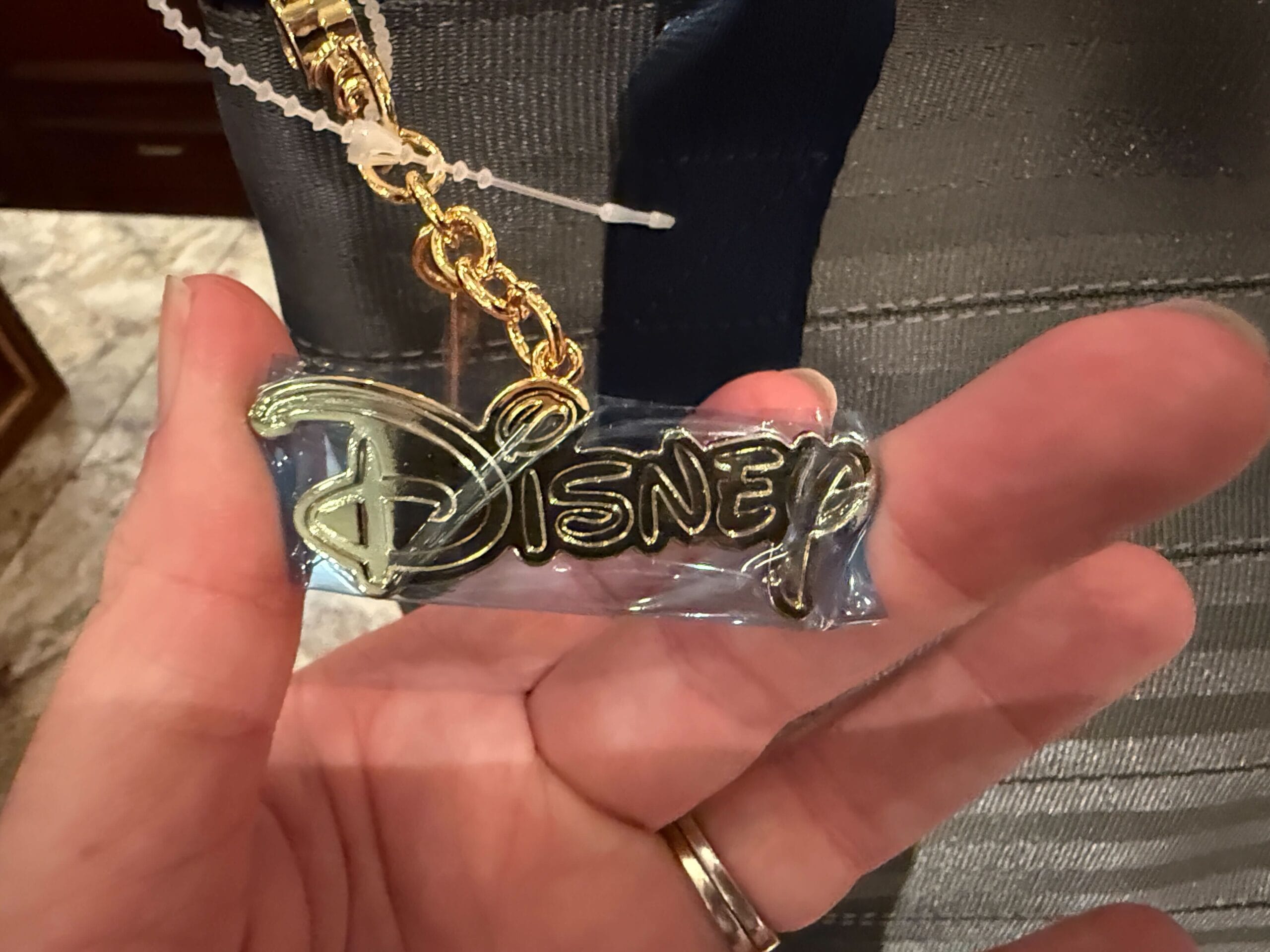 A hand holds a gold Disney logo keychain attached to a zipper pull.